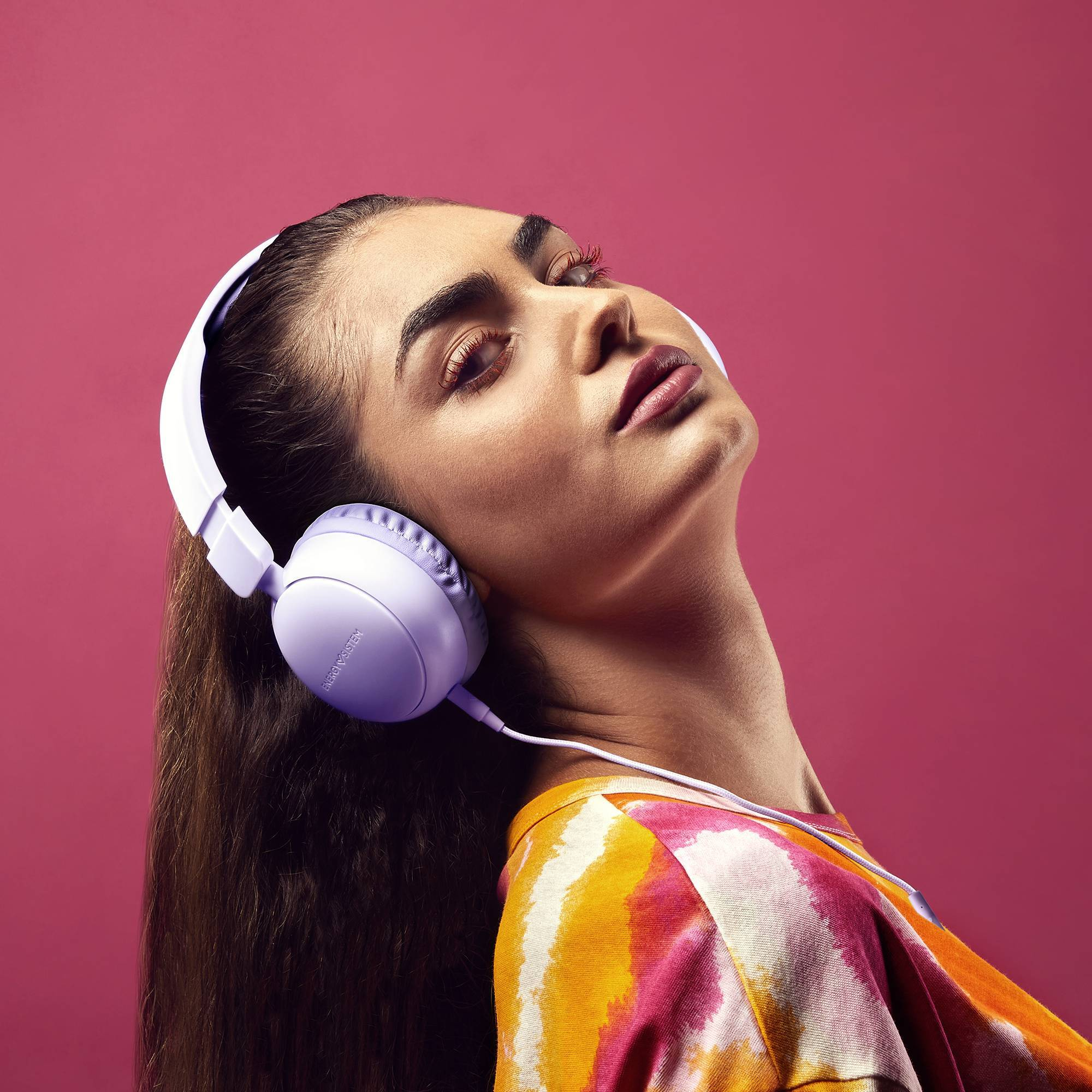 Kobieta w białych słuchawkach, patrząca w górę, różowe tło.