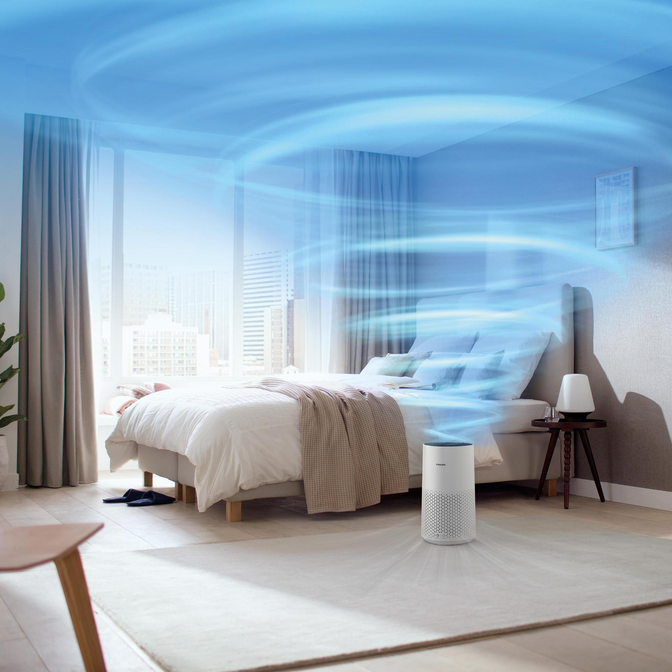 Ein Schlafzimmer mit einem Luftreiniger, der blaue Luftströmungen aussendet, einem Bett und einem Fenster.
