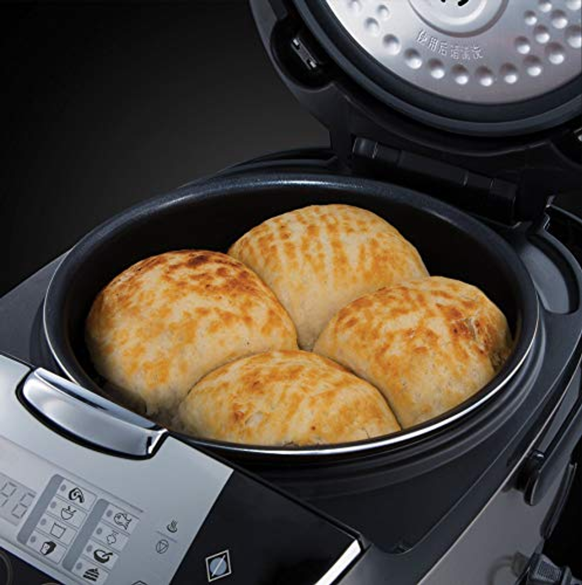 Gros plan d'un cuiseur à riz avec quatre petits pains cuits au four à l'intérieur.