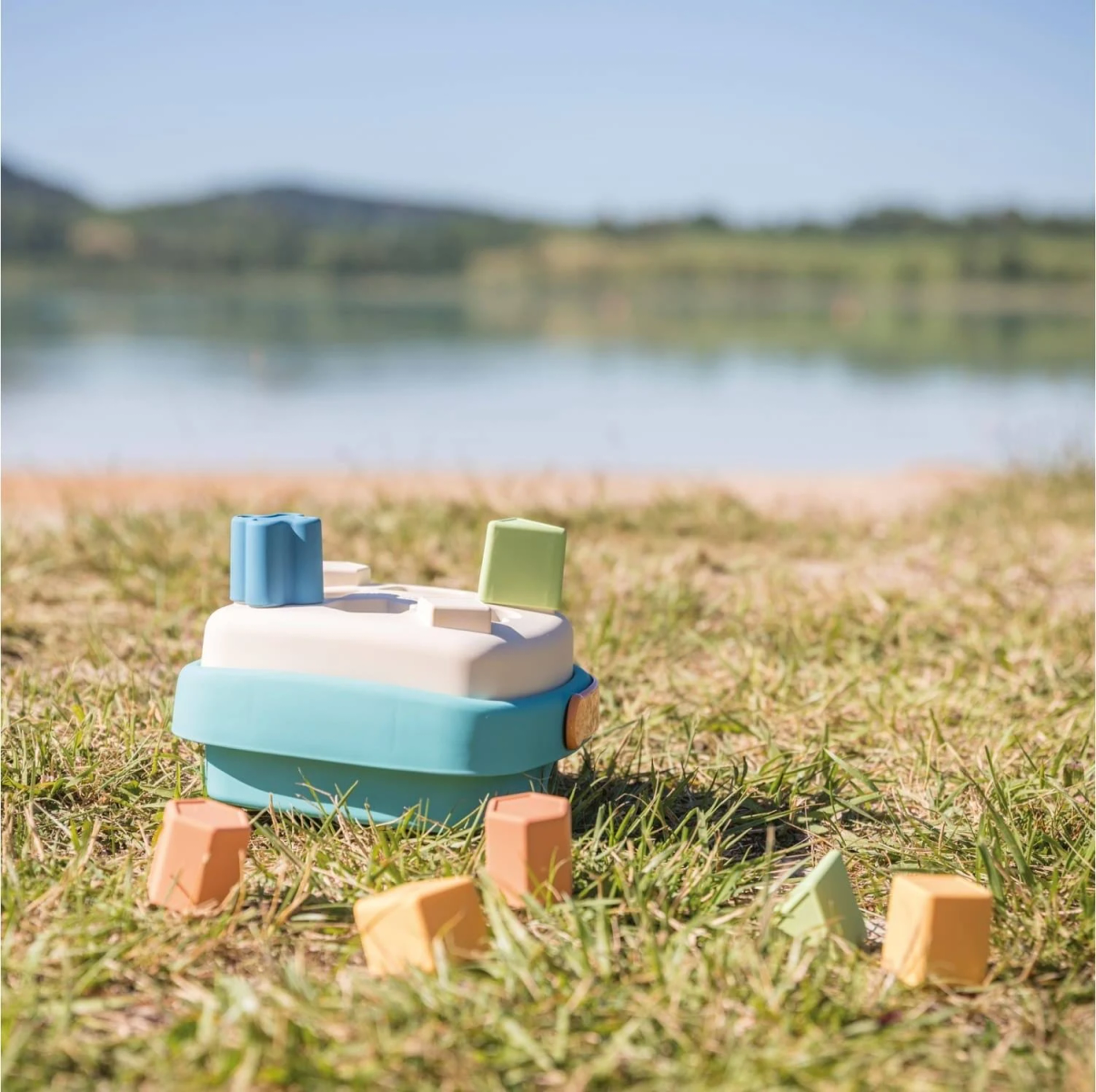 Ein buntes Spielzeugboot mit Formen auf Gras, mit einem See im Hintergrund.