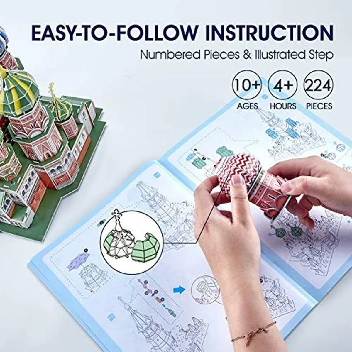 Hände, die ein Modell eines Gebäudes zusammenbauen. Anleitung und Modellteile sichtbar.