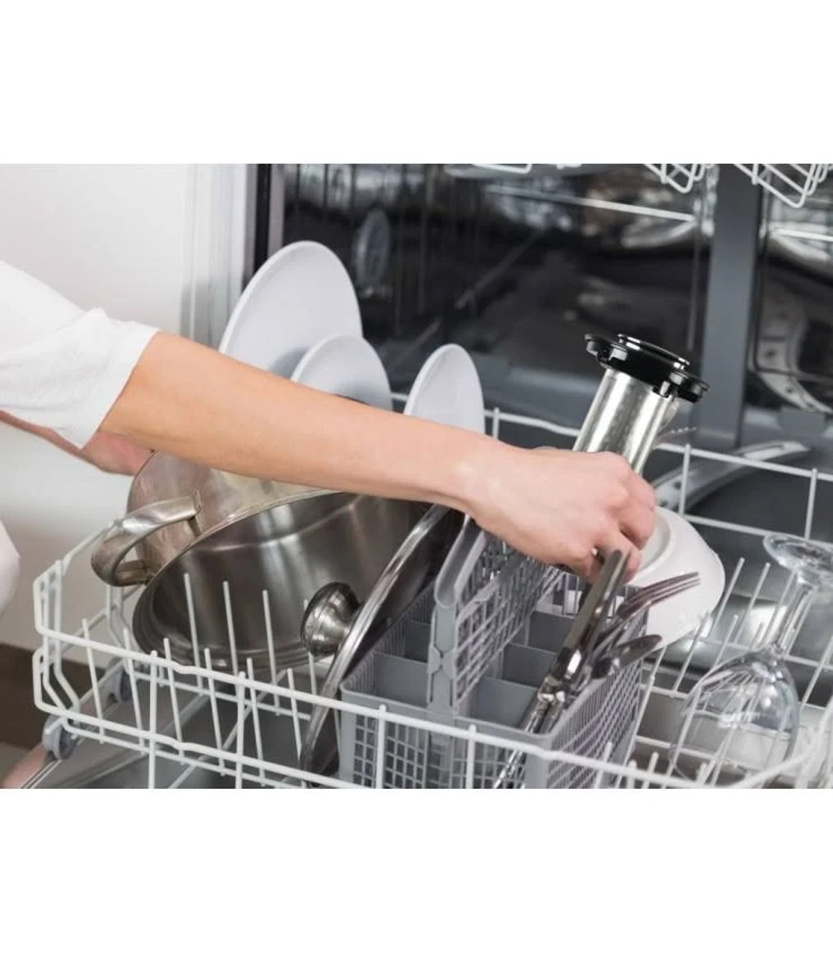 Osoba załadowuje zmywarkę. Wkładają garnki, naczynia i sztućce do koszy.