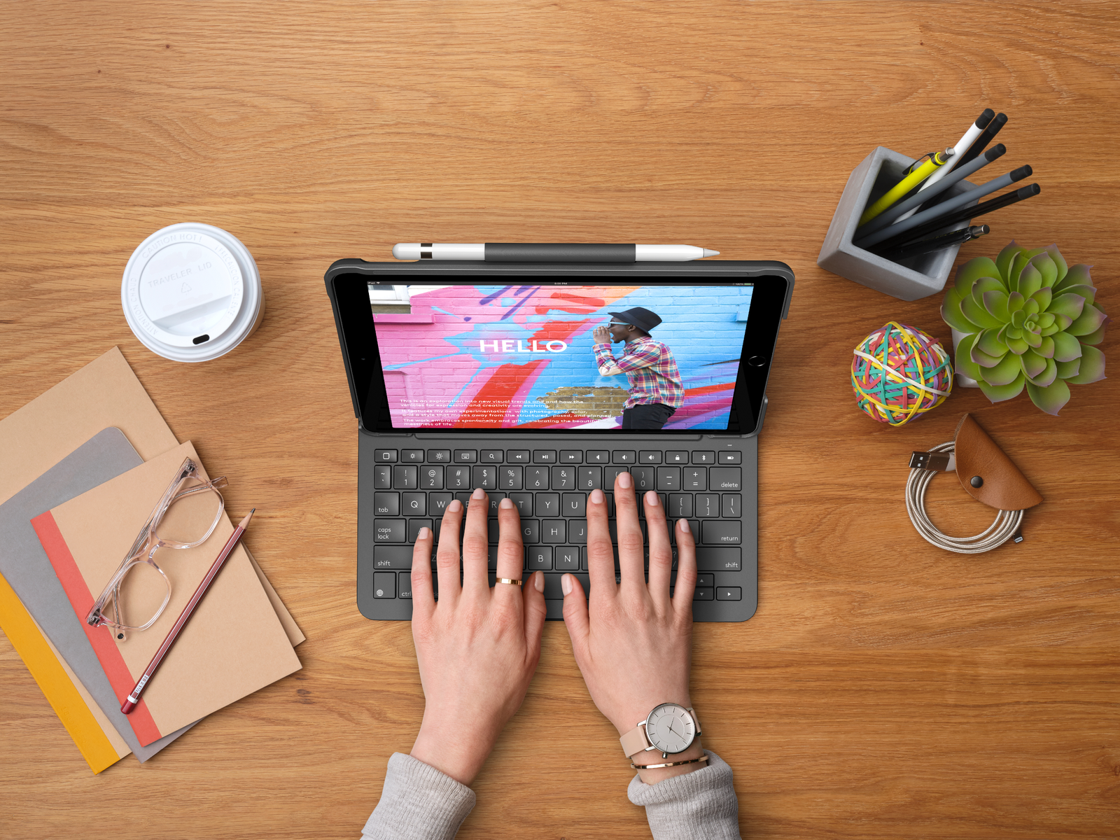 Hände tippen auf einer Tastatur, die an ein Tablet angeschlossen ist. Andere Elemente sind eine Kaffeetasse und eine Brille.