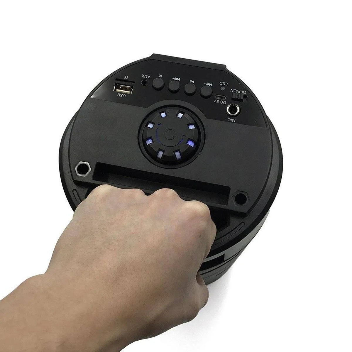 Schwarzer Lautsprecher mit Bedientasten und einer Hand, die ihn hält. USB-, AUX- und Mikrofonanschlüsse sind sichtbar.