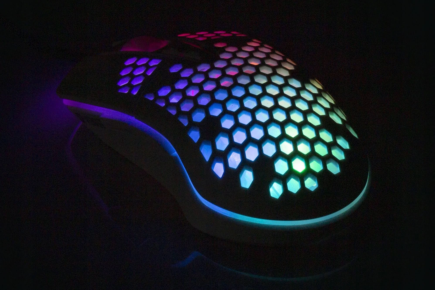 Eine Gaming-Maus mit Wabenmuster, die auf dunklem Hintergrund mit farbenfrohen Lichtern beleuchtet ist.