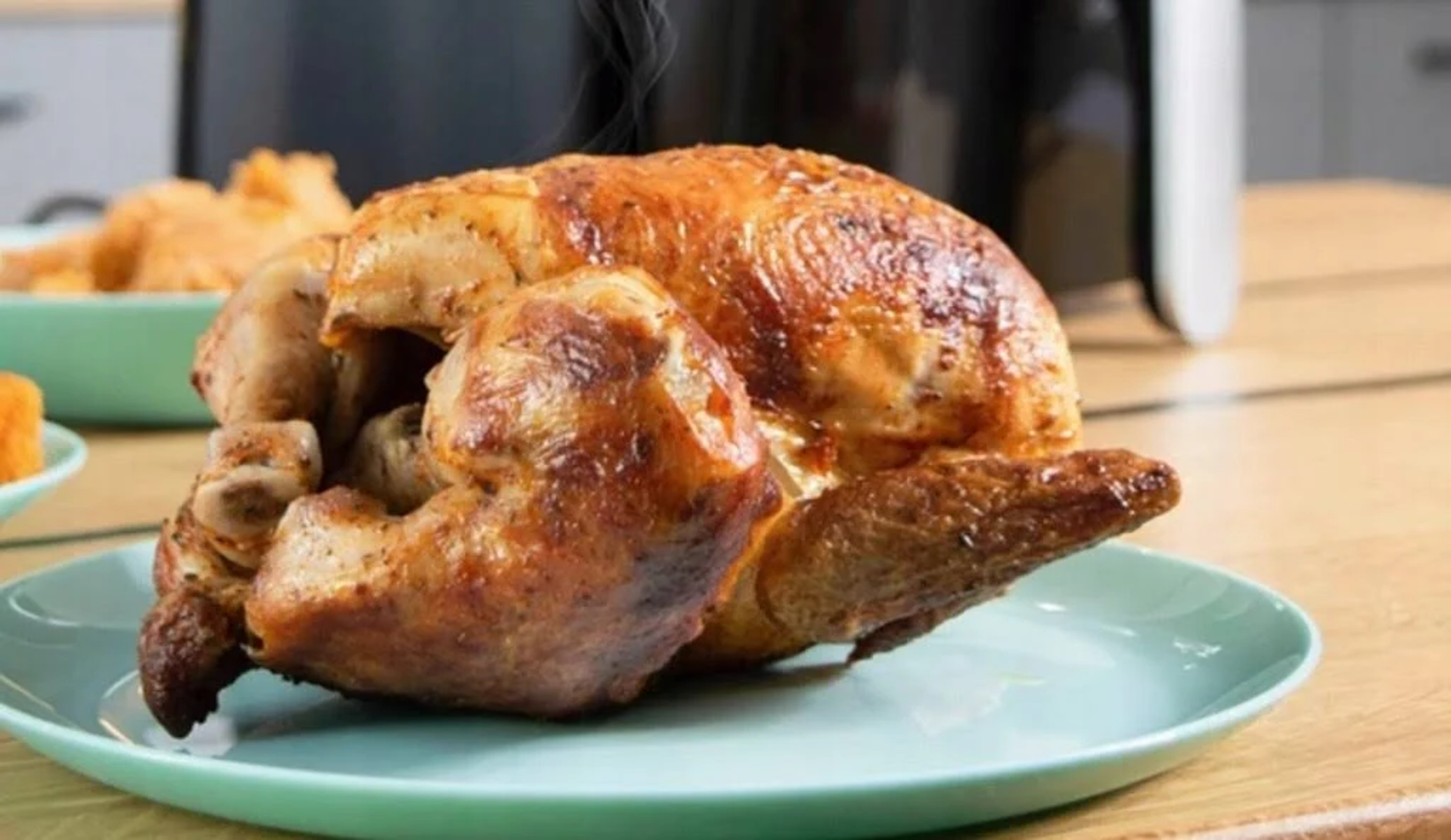 Gebratenes Huhn auf einem tealfarbenen Teller. Seitenansicht des Huhns, mit unscharfem Essen im Hintergrund.