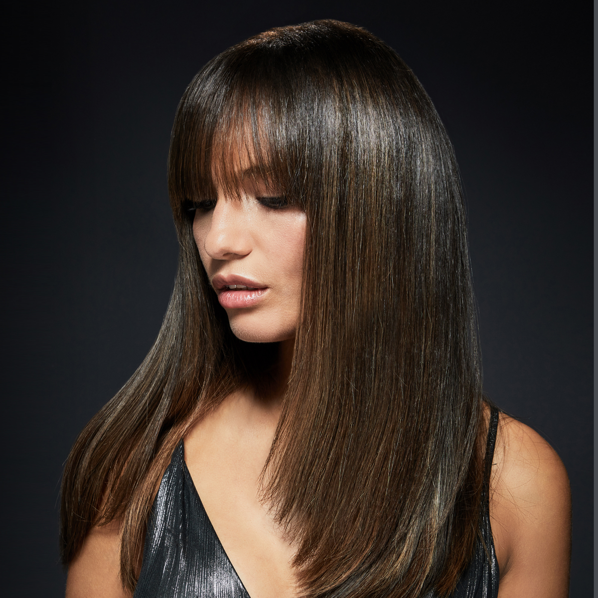 Una donna con capelli castano scuro e lisci e una frangia, con un top nero che guarda verso il basso.