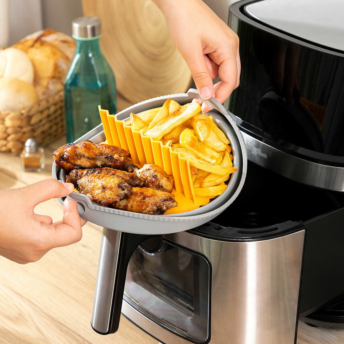 Mani che tengono un vassoio di cibo sopra una friggitrice ad aria, con patatine fritte e pollo.