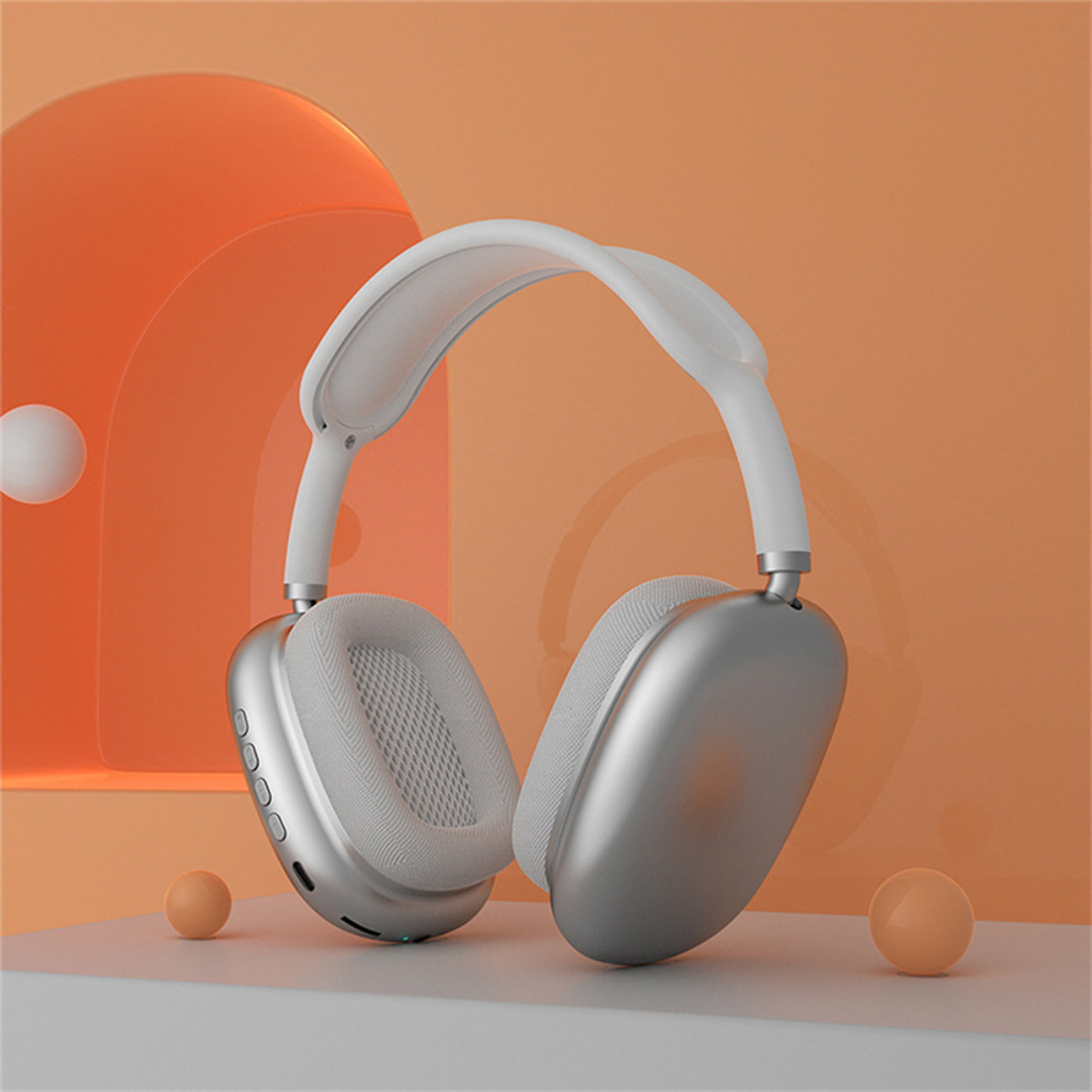 Auriculares Apple AirPods Max plateados sobre una superficie blanca con fondo y bolas naranjas.
