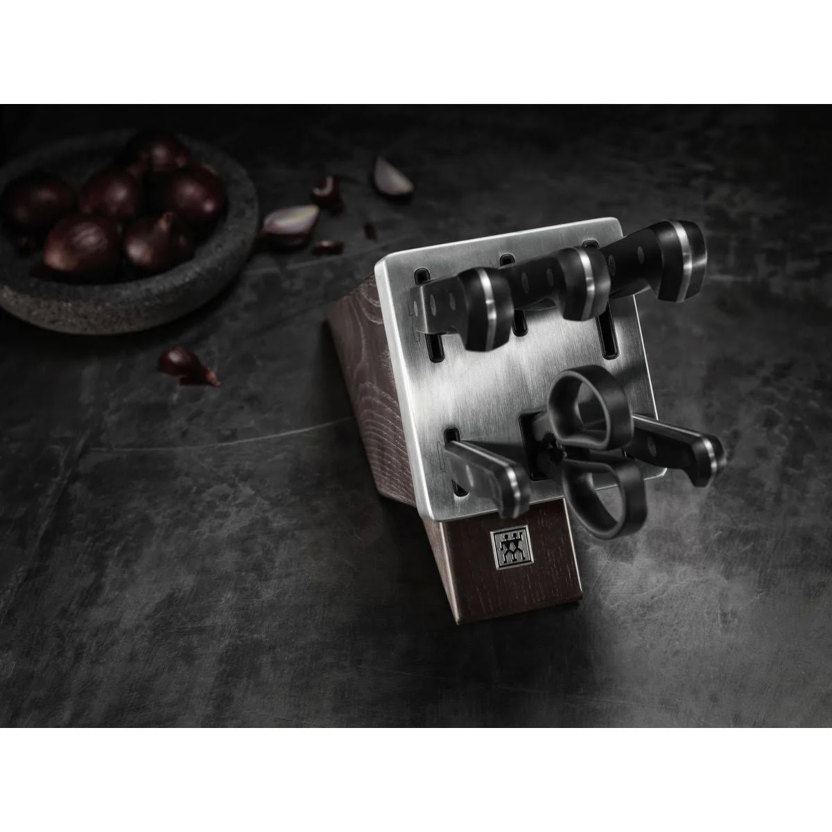 Blok na noże z nożami. Czarne uchwyty i ostrza ze stali nierdzewnej. Ciemna powierzchnia z jedzeniem.