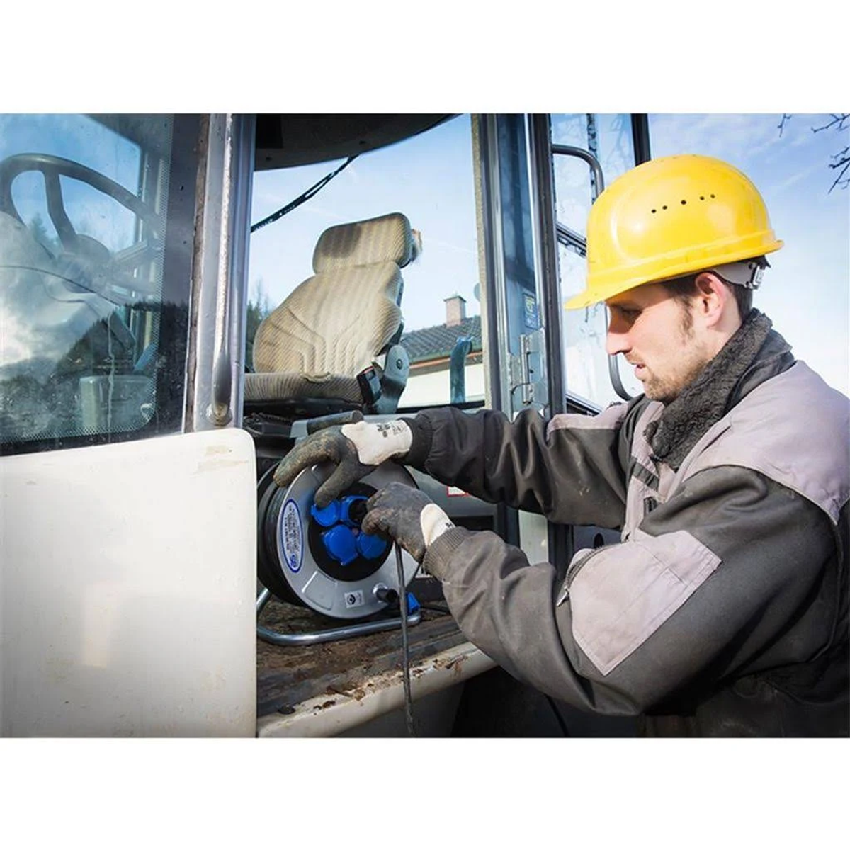Arbeiter mit gelbem Helm verbindet Stromkabel mit einer Kabeltrommel am Fahrzeug.
