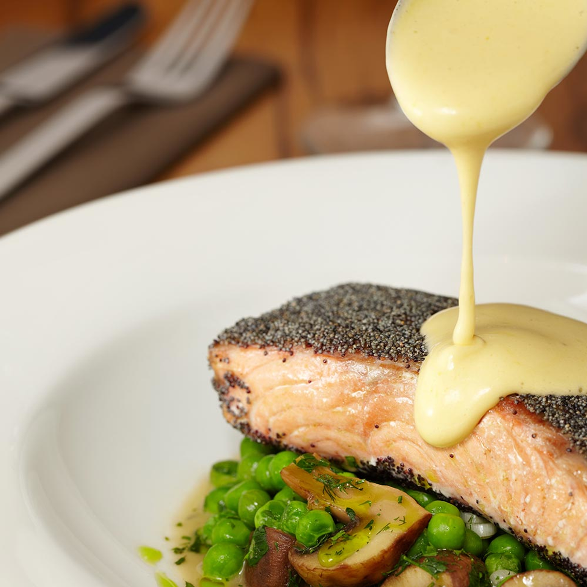 Łosoś z sosem polewanym na wierzchu, podany z groszkiem i grzybami na talerzu.