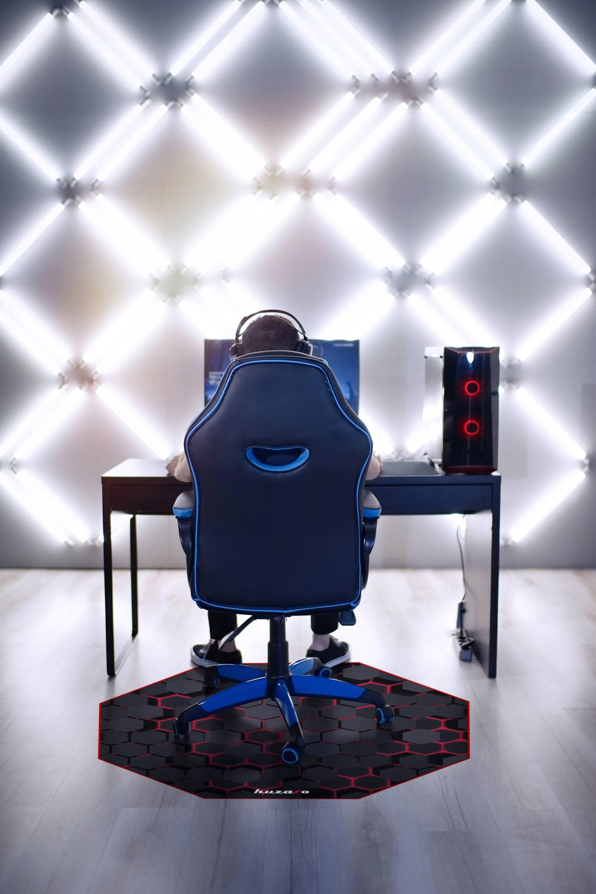 Eine Person spielt, sitzt in einem blau-schwarzen Stuhl, mit Gaming-Setup und einer sechseckigen Matte.