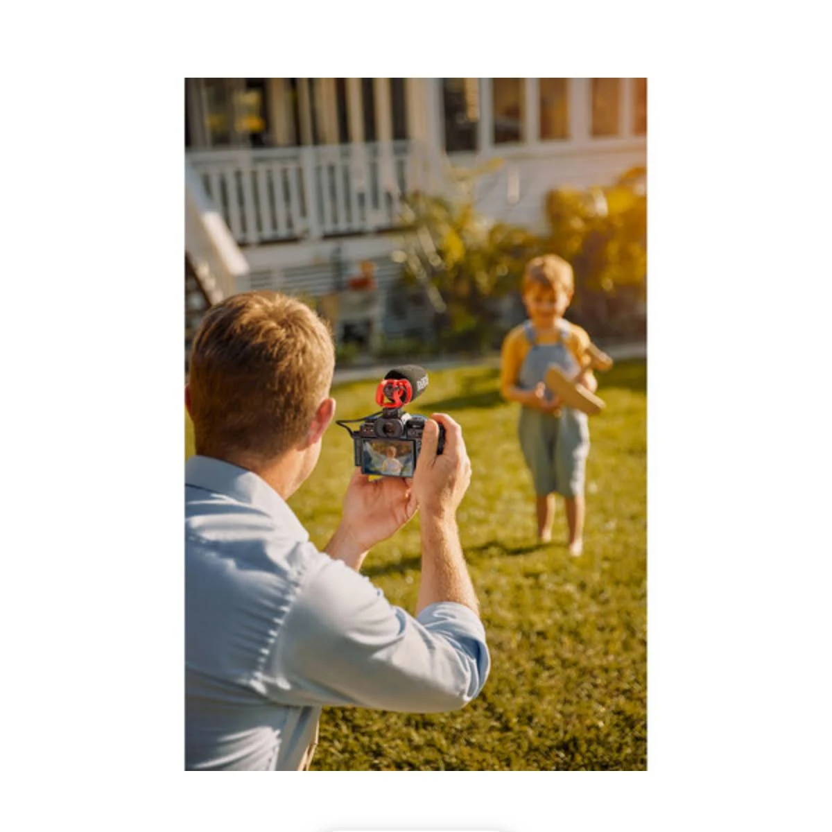 Mann filmt Kind mit Kamera. Kind hält Spielzeugflugzeug im sonnigen Garten.