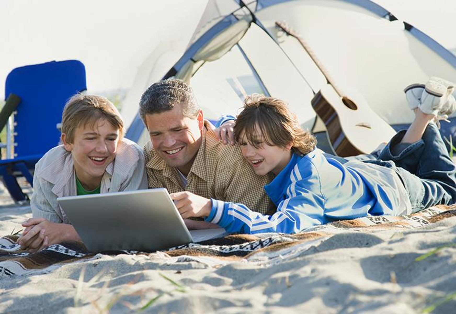Familie beim Camping. Vater und zwei Söhne benutzen einen Laptop auf einer Decke.