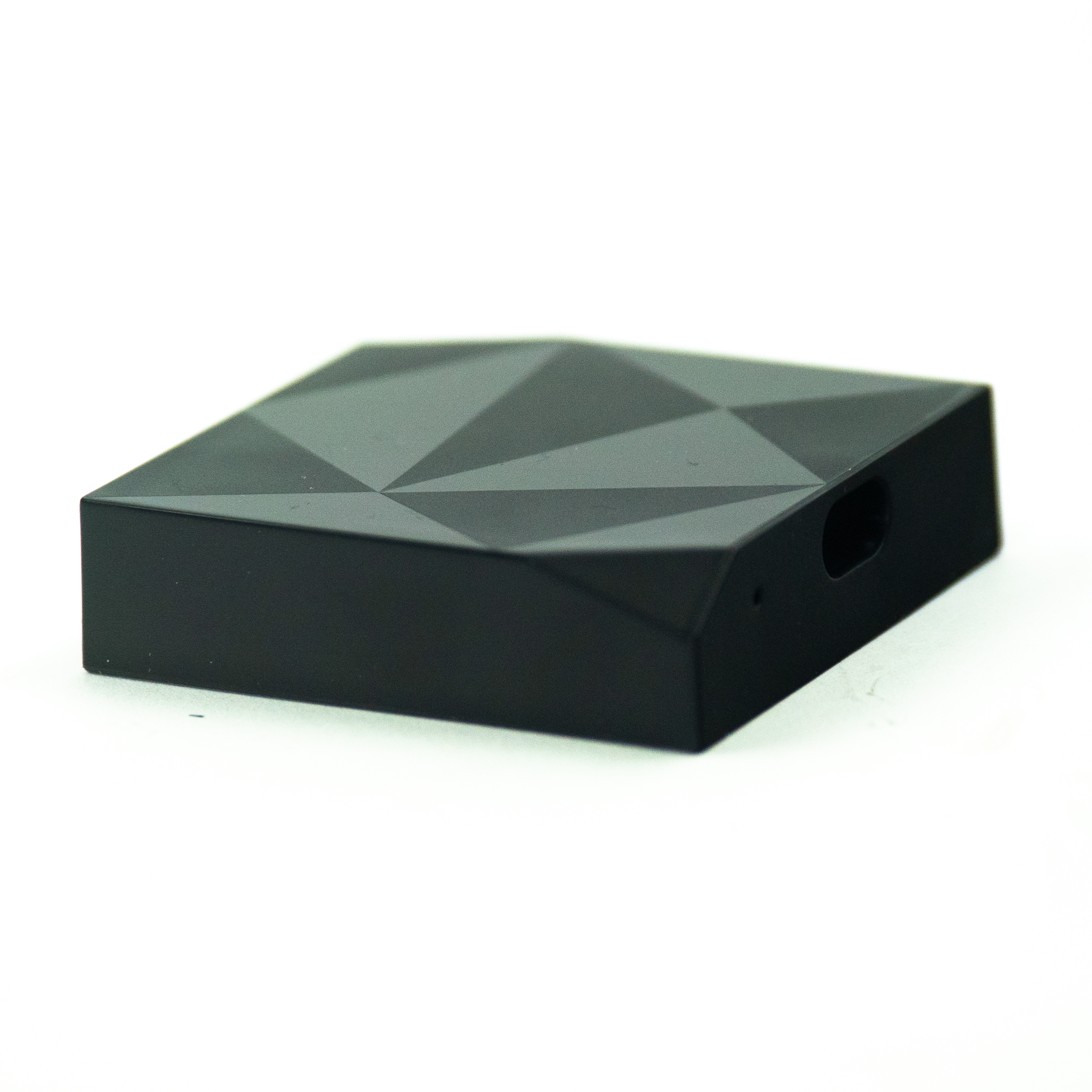 Ein schwarzes Gerät mit geometrischem Muster. Es ist quadratisch, leicht abgewinkelt und hat ein Loch.