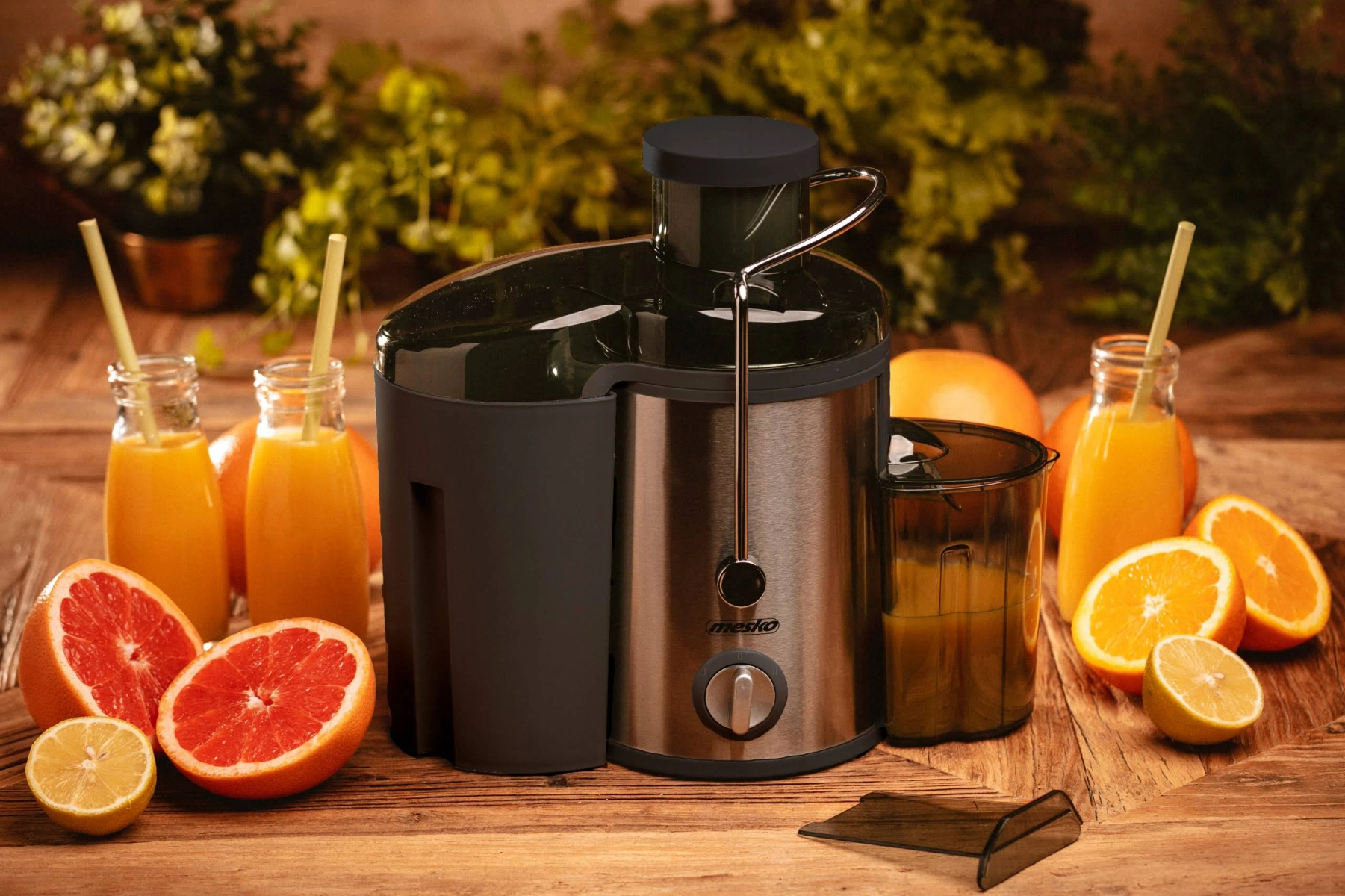 Centrifuga con succo d'arancia e frutta su tavolo di legno. Verde sullo sfondo.