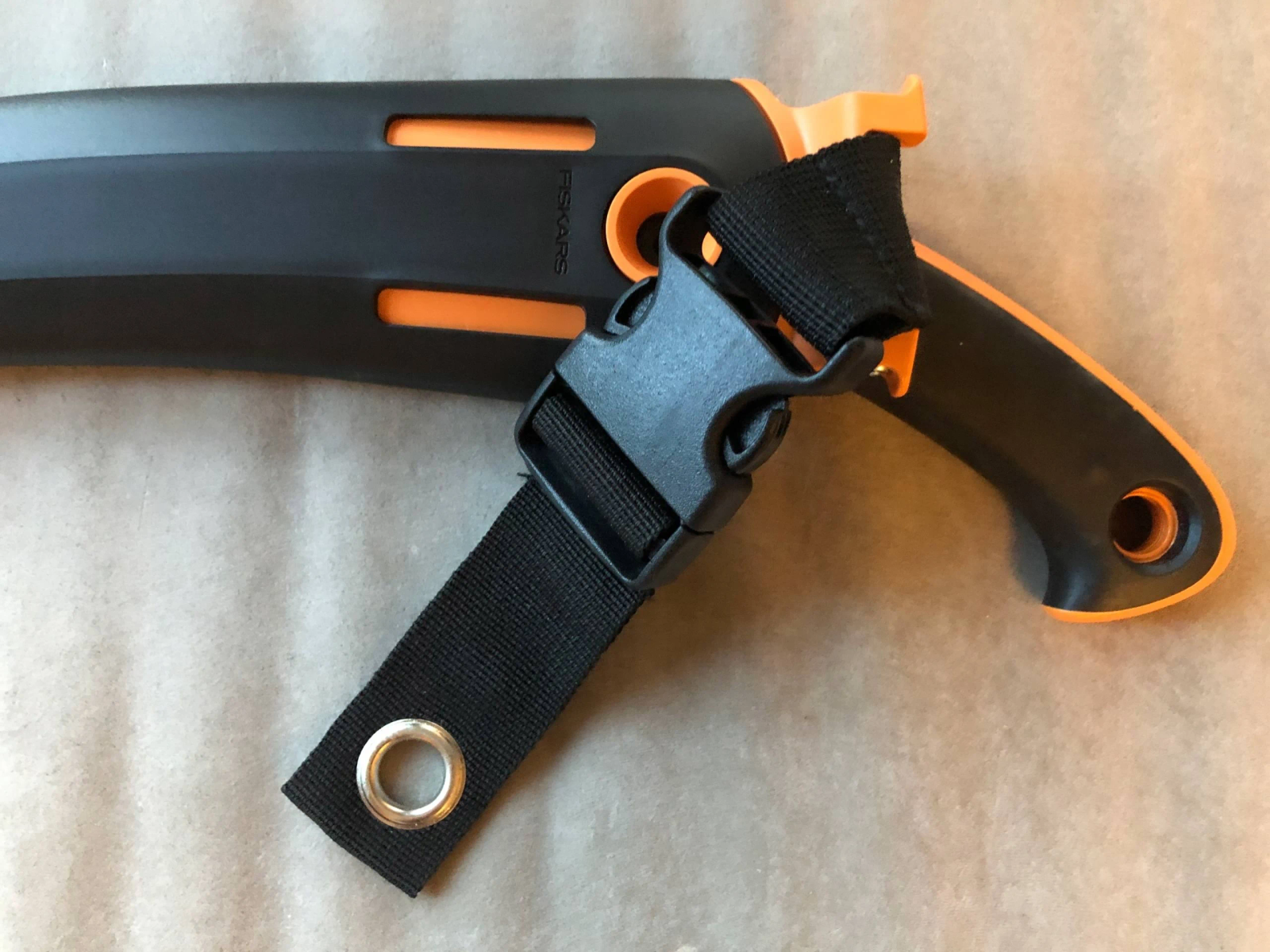 Orange und schwarze Säge mit schwarzem Riemenansatz auf braunem Untergrund.