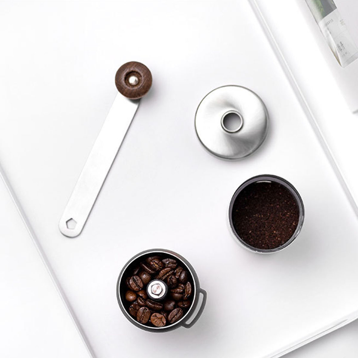 Kaffeemühlen-Teile auf einem weißen Tablett. Enthält Bohnen, Kaffeepulver, eine Mühle und ihren Deckel.