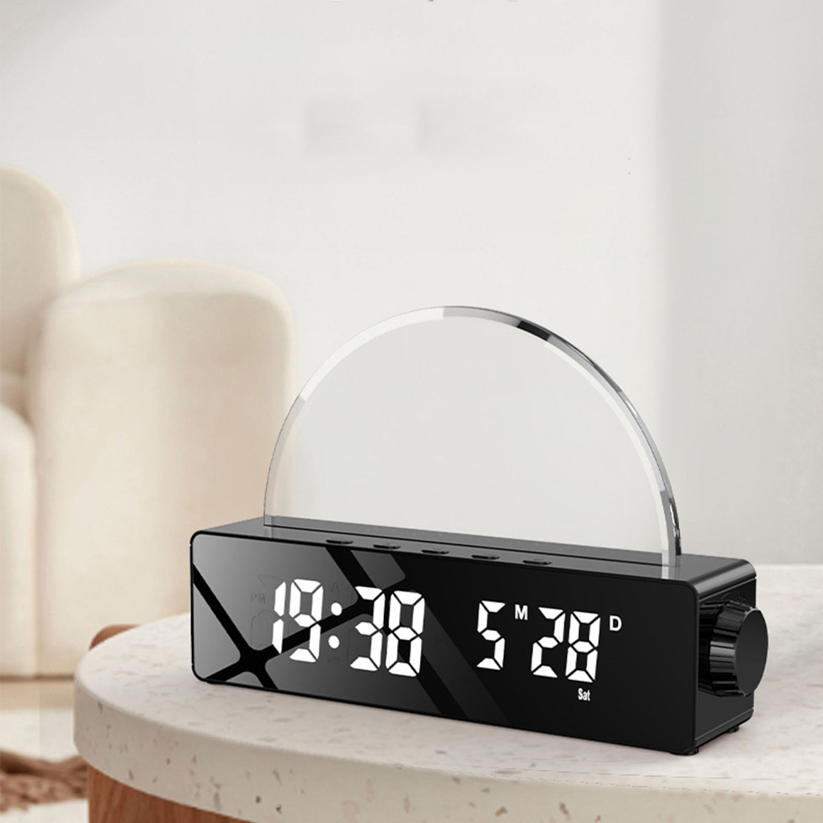 Schwarze Digitaluhr. Sie zeigt Zeit und Datum an. Ein gebogenes Licht befindet sich darüber auf einem weißen Tisch.