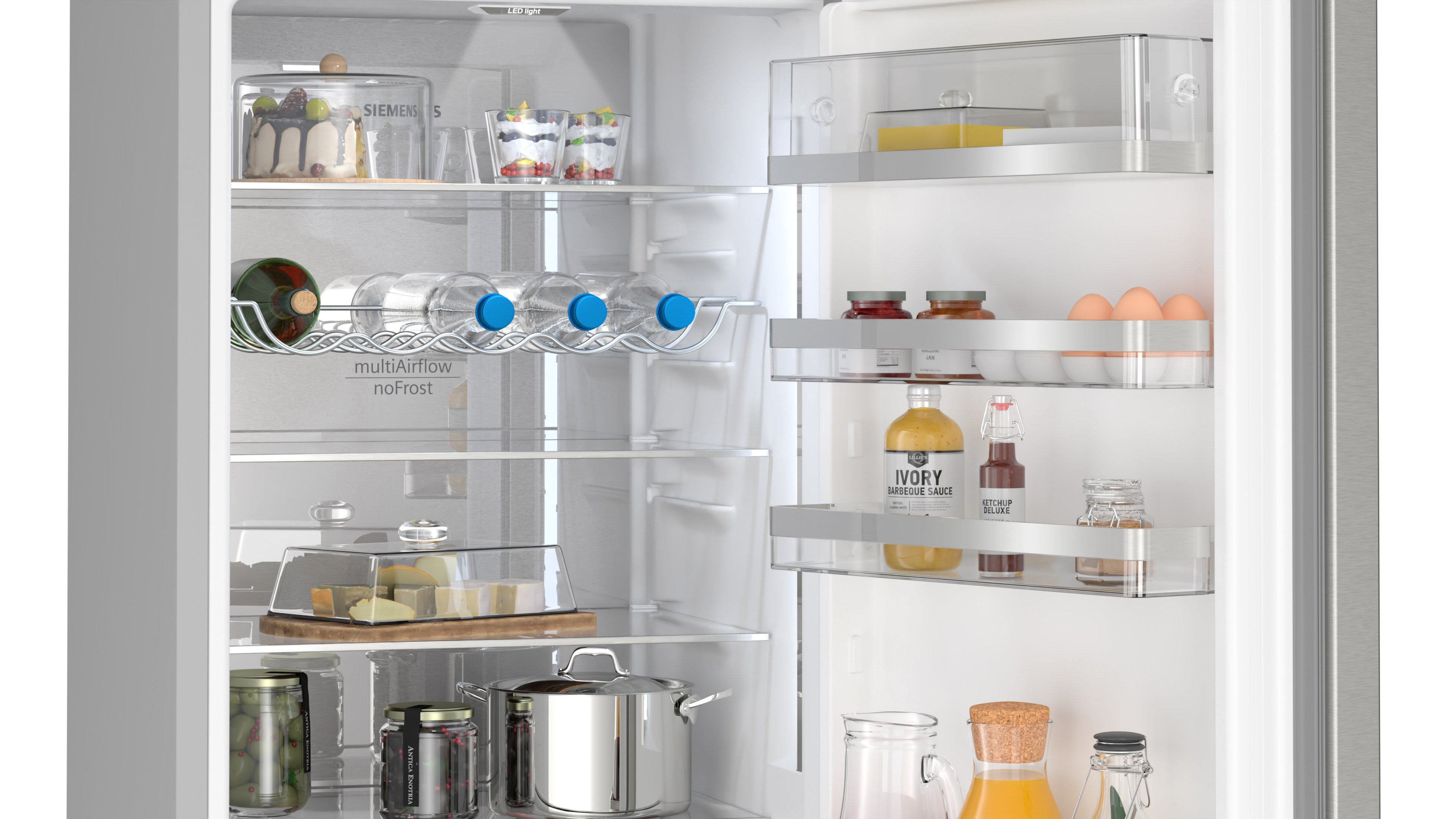 Refrigerador abierto con alimentos: pasteles, bebidas, queso, frascos y huevos en estantes. Acabado de acero inoxidable.