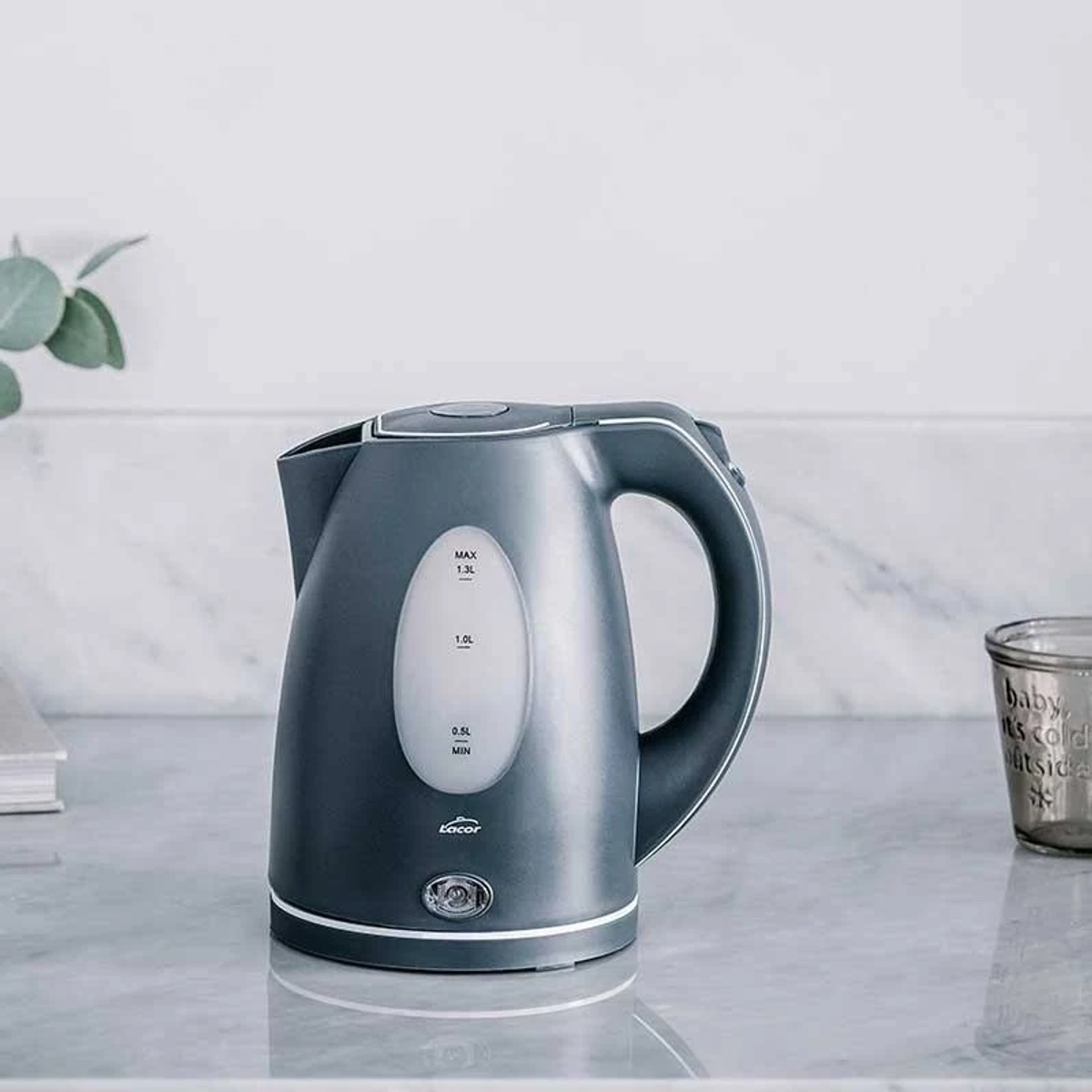 Un bollitore elettrico grigio con indicatore del livello dell'acqua. Su una superficie riflettente.