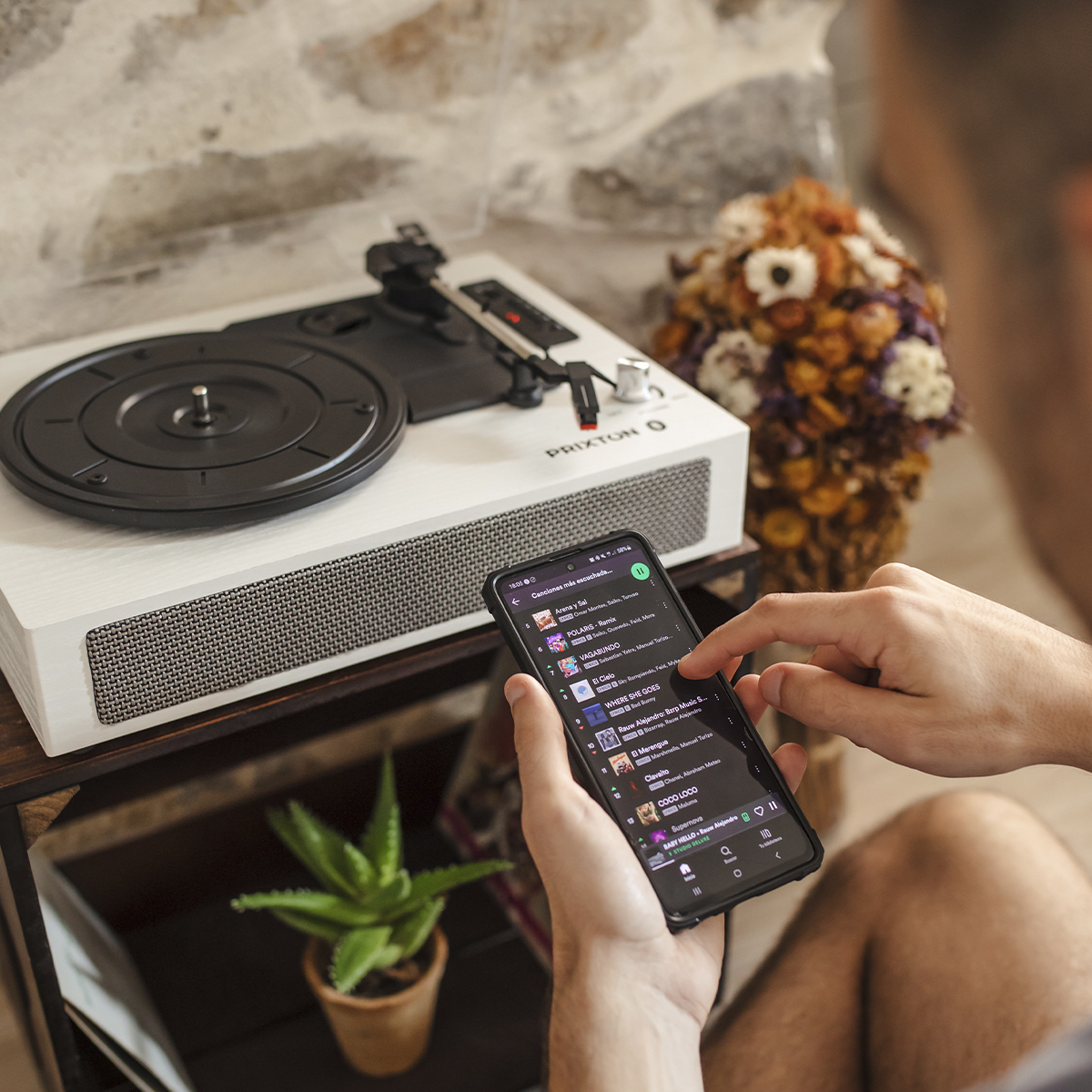 Mężczyzna korzysta ze smartfona. Gramofon i roślina w tle.