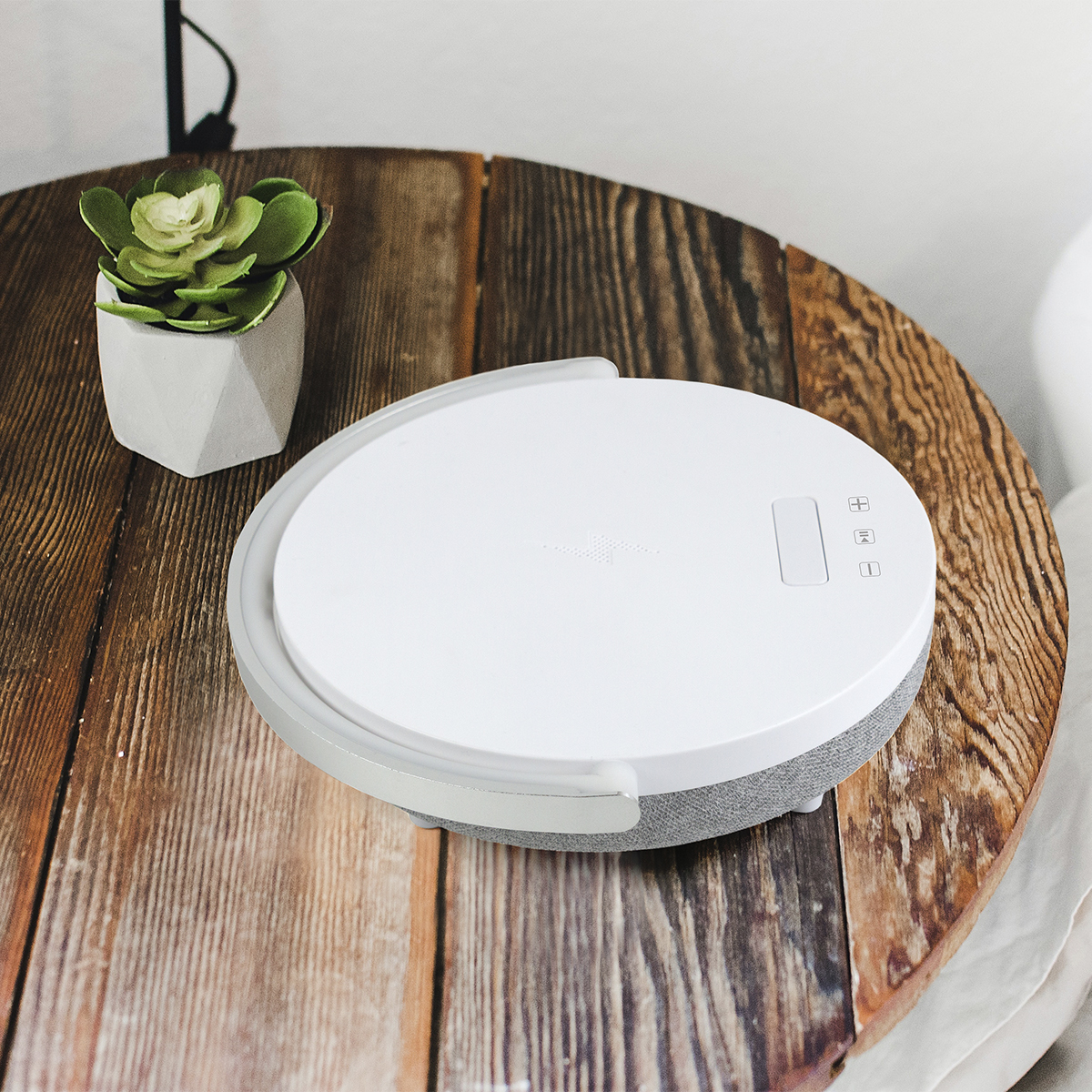 Białe urządzenie na drewnianym stole obok sukulentu w białej doniczce.