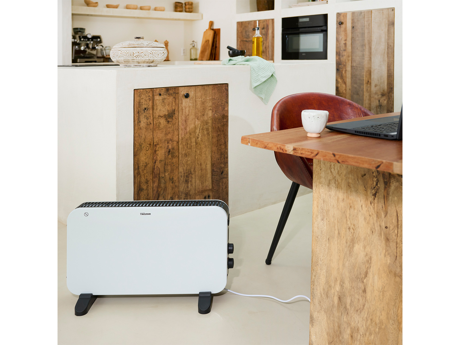 Un riscaldatore bianco in un ambiente cucina, con un tavolo di legno e un laptop.