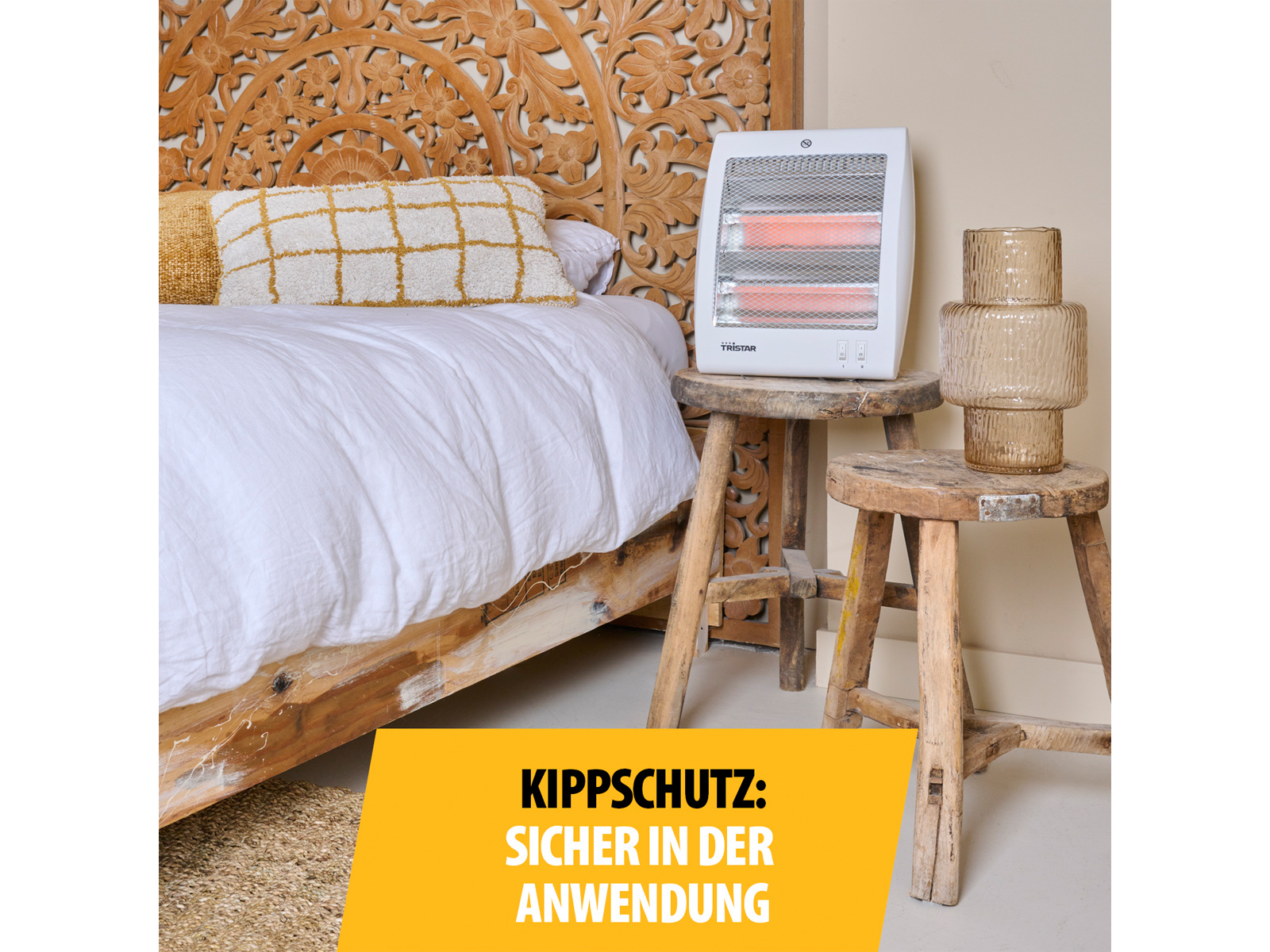 Ein weißer Elektroheizer auf einem Holzschemel, in der Nähe eines Bettes mit geschnitztem Kopfteil und gelbem Schild.