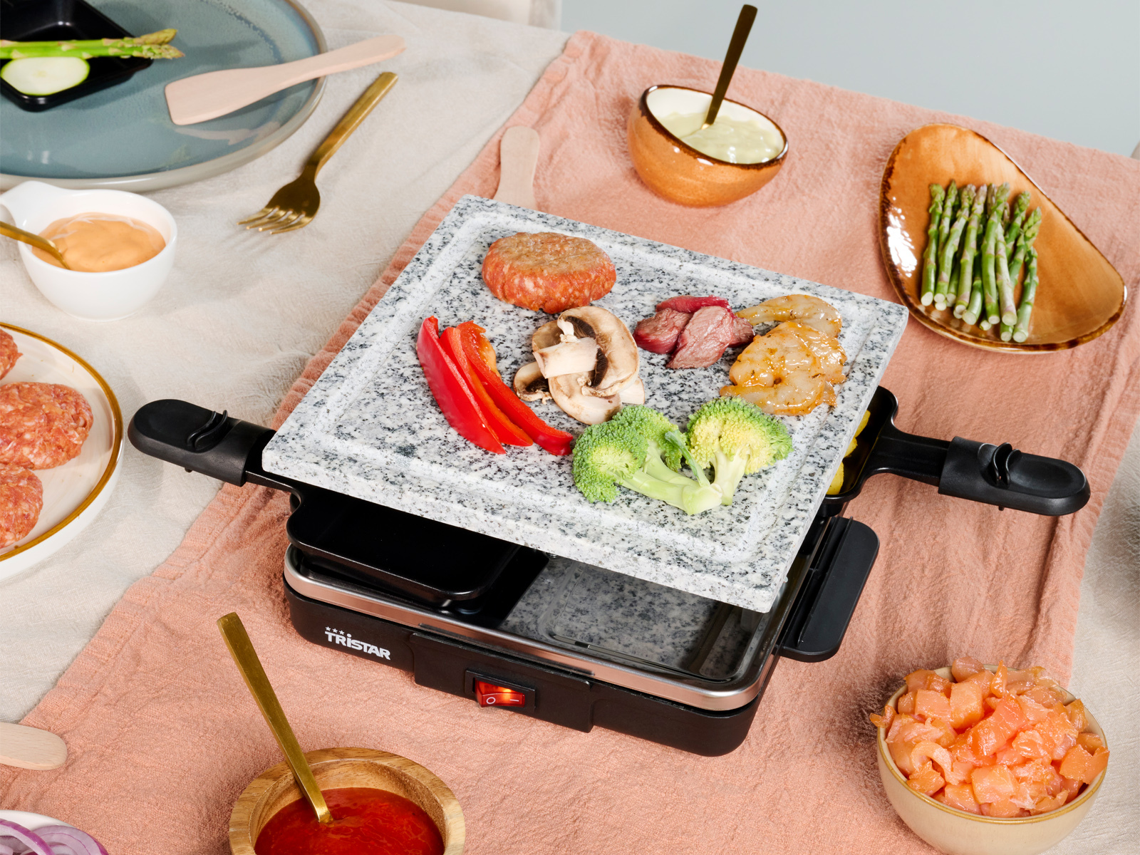 Raclette-Grill mit gekochtem Essen: Fleisch, Gemüse und Käse. Serviert mit Saucen und Utensilien.