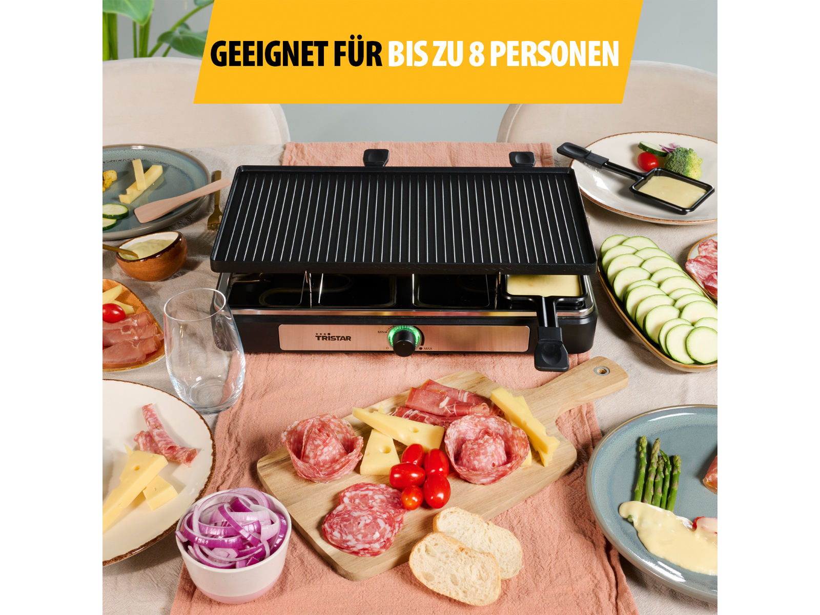 Una griglia per raclette con cibo su un tavolo. Include formaggio, carni e verdure pronte per essere grigliate.