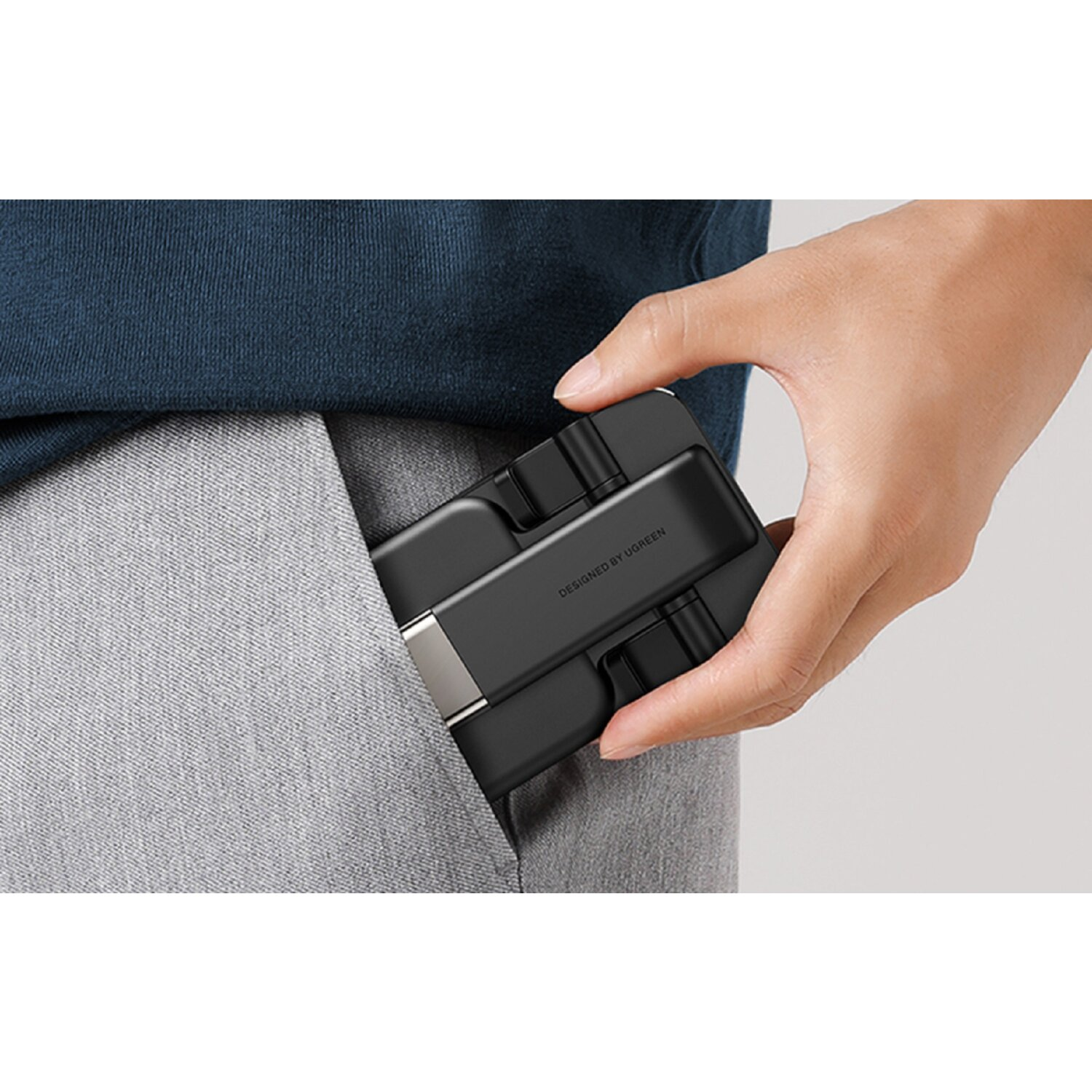 Eine Hand steckt einen schwarzen USB-Hub in eine graue Hosentasche.
