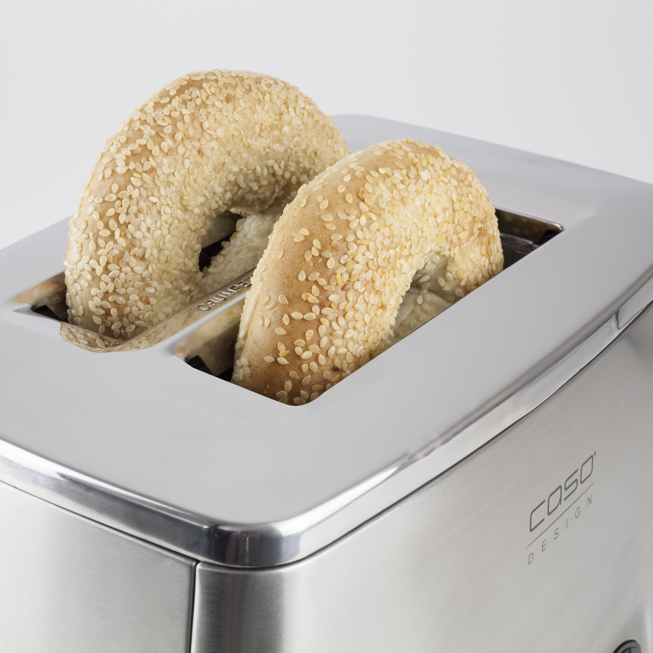 Una tostadora de acero inoxidable con dos bagels dentro, sobre una superficie blanca.