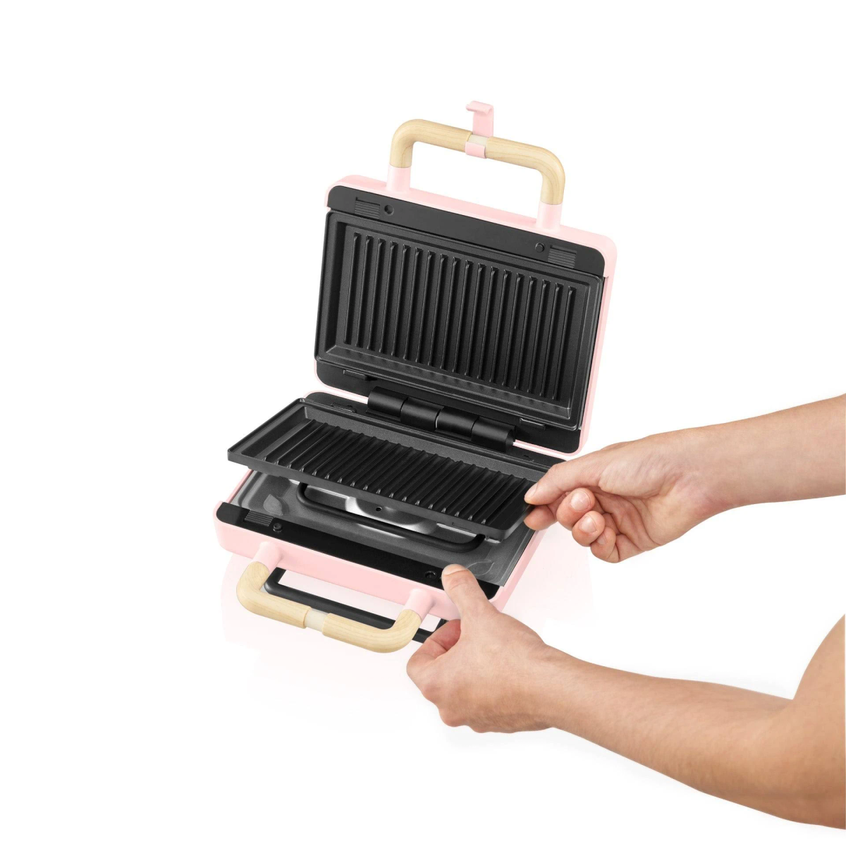Máquina para sándwiches rosa siendo ensamblada. Manos sujetan una placa caliente.