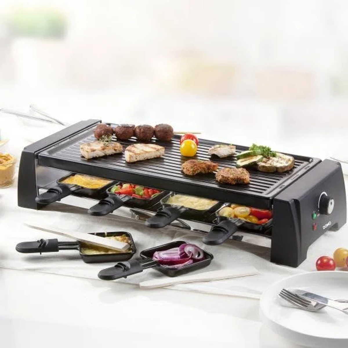Una parrilla raclette con varios alimentos cocinados, incluyendo verduras y carnes, sobre una superficie blanca.