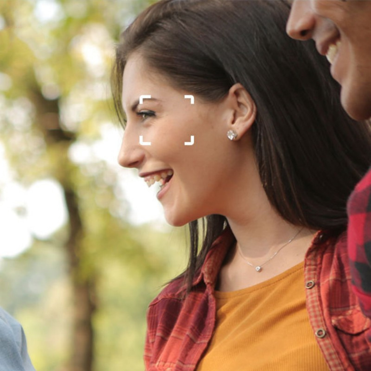 Kobieta śmieje się, widok z profilu, w pomarańczowym topie i czerwonej koszuli w kratę. Kwadrat ostrości na jej twarzy.