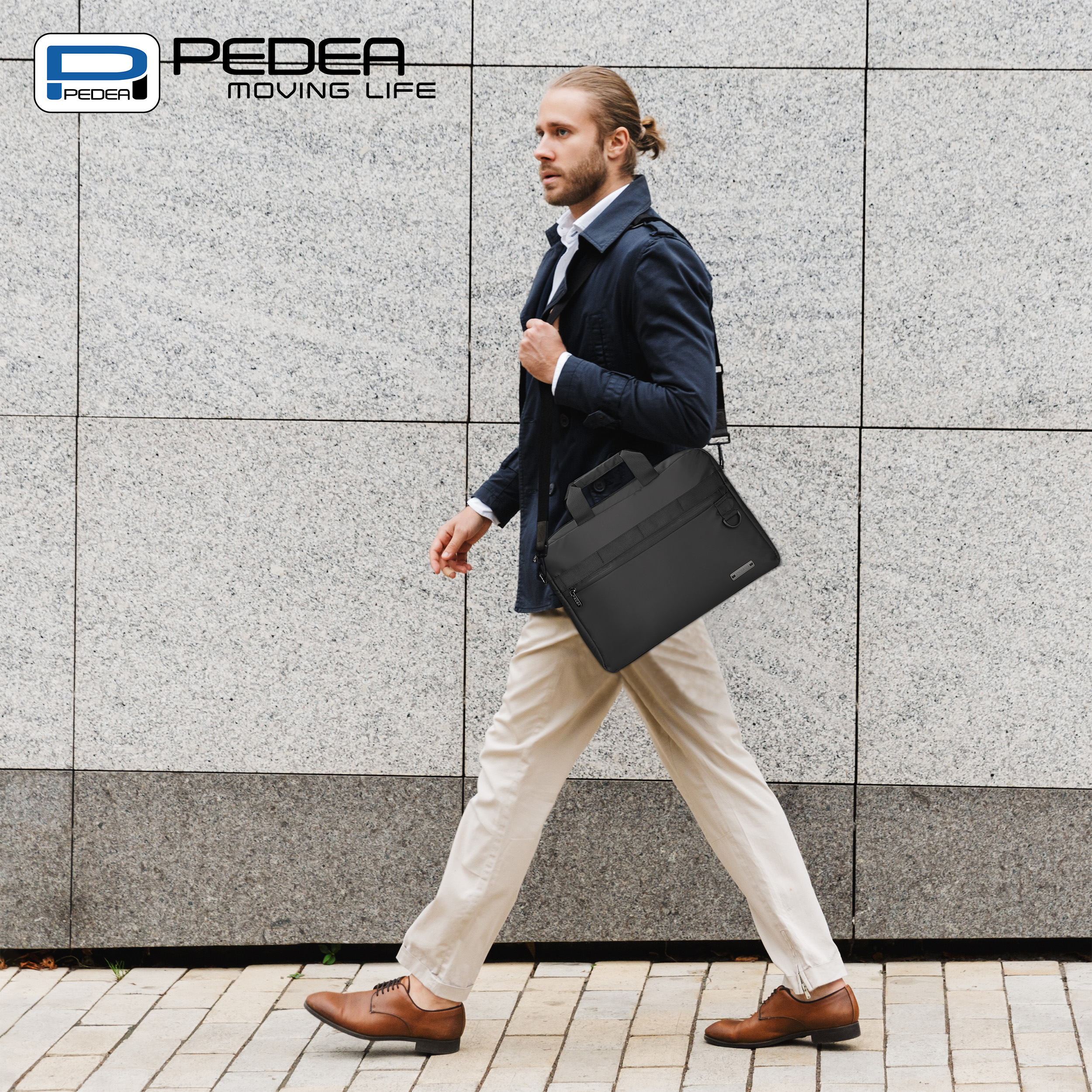 Ein Mann trägt eine schwarze Tasche, geht auf dem Bürgersteig, mit grauem Wandhintergrund.