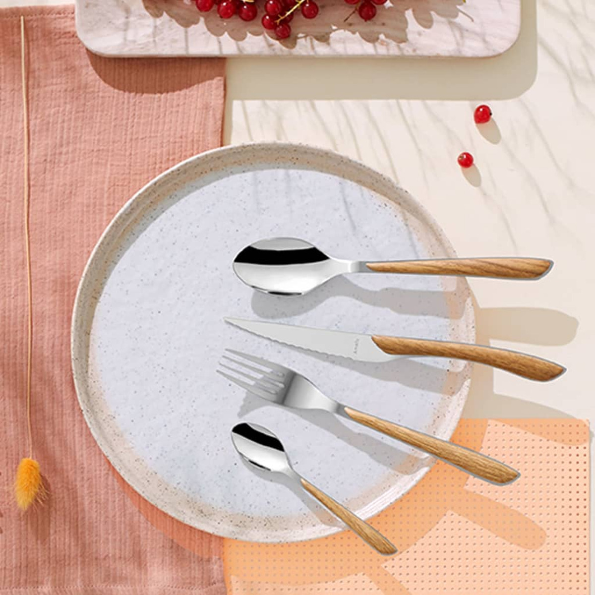 Tischarrangement: Teller mit Besteck, Löffel, Gabel und Messer. Rote Beeren und rosa Serviette.