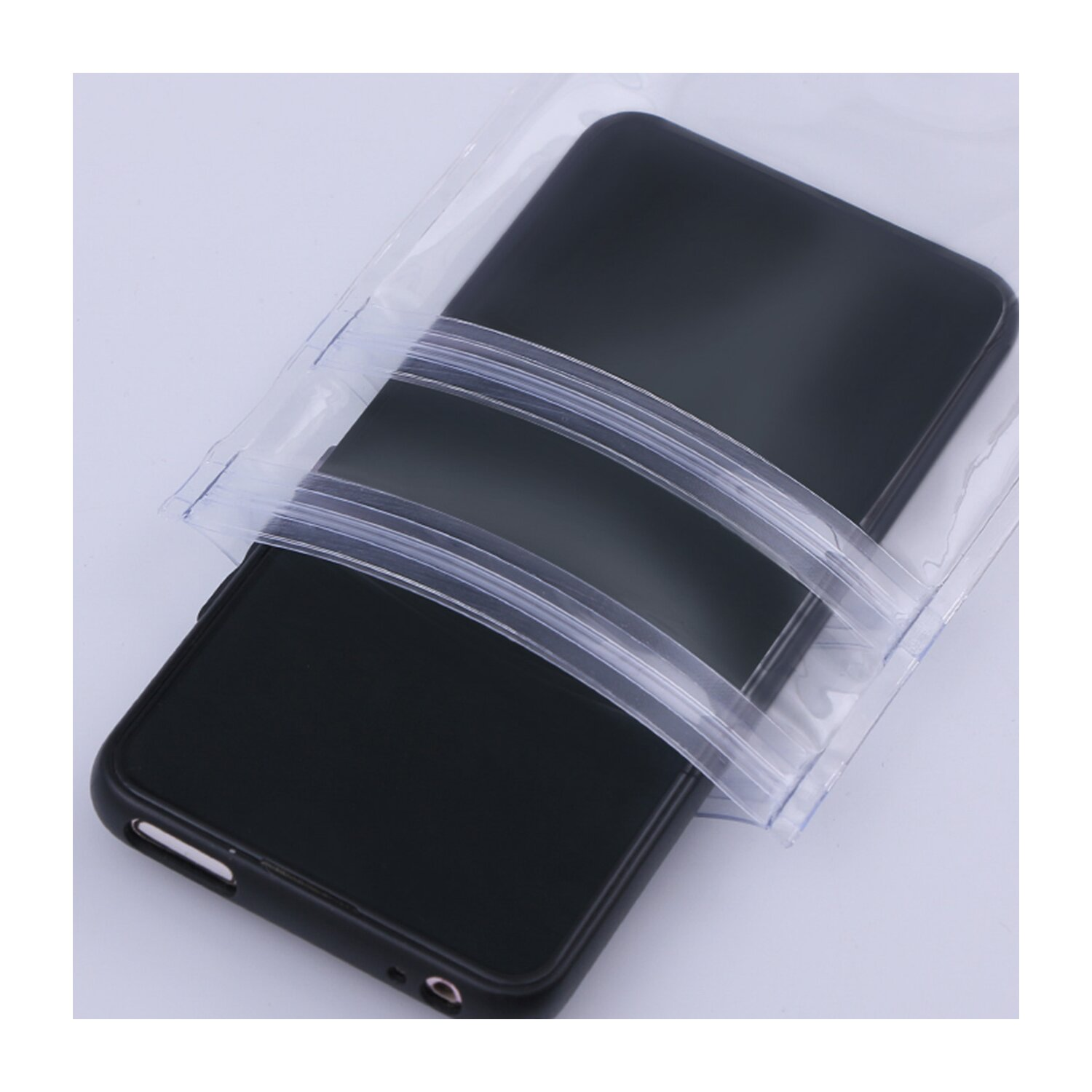 Schwarzes Smartphone in einer durchsichtigen Plastiktüte. Weißer Hintergrund.