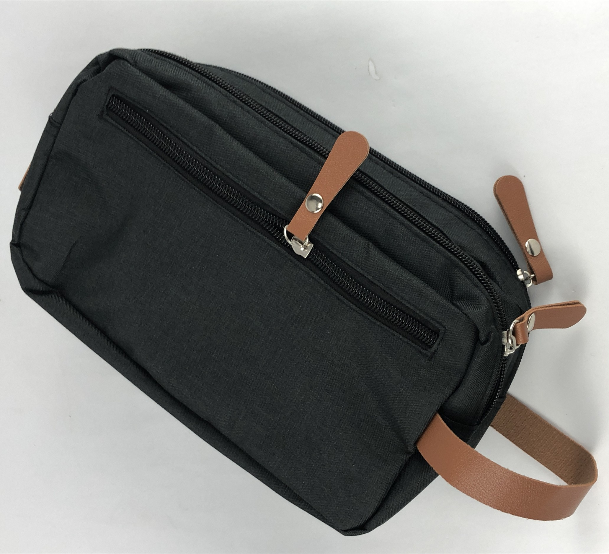 Une trousse de toilette gris foncé avec des accents de cuir marron, avec des fermetures éclair et des poignées en cuir, fond blanc.