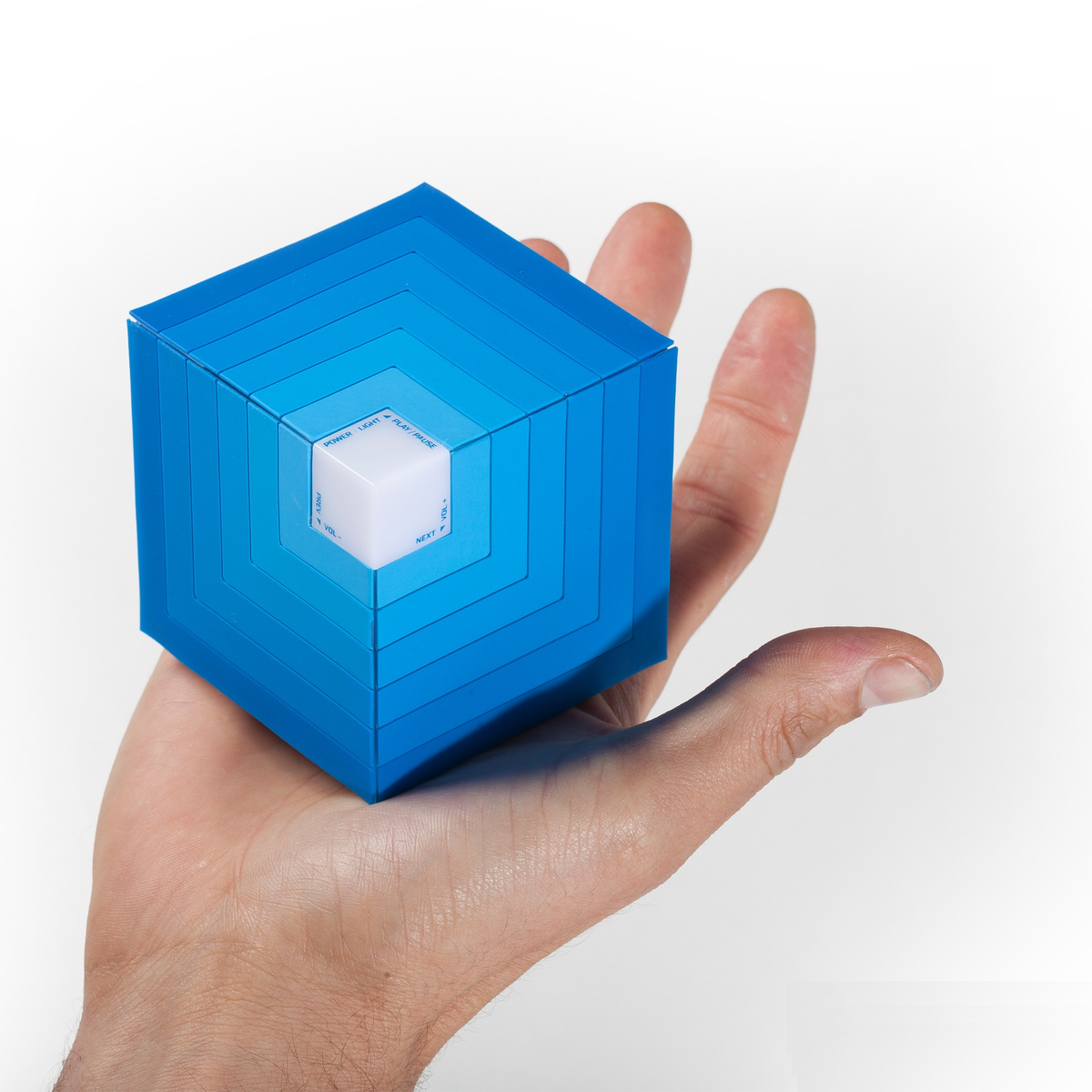 Cubo azul sostenido por una persona. El cubo tiene capas y diferentes palabras como POWER y VOL. Fondo blanco.