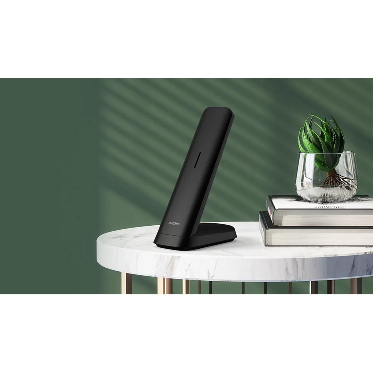 Soporte de carga inalámbrica Philips negro sobre mesa mármol, junto a planta en jarrón.