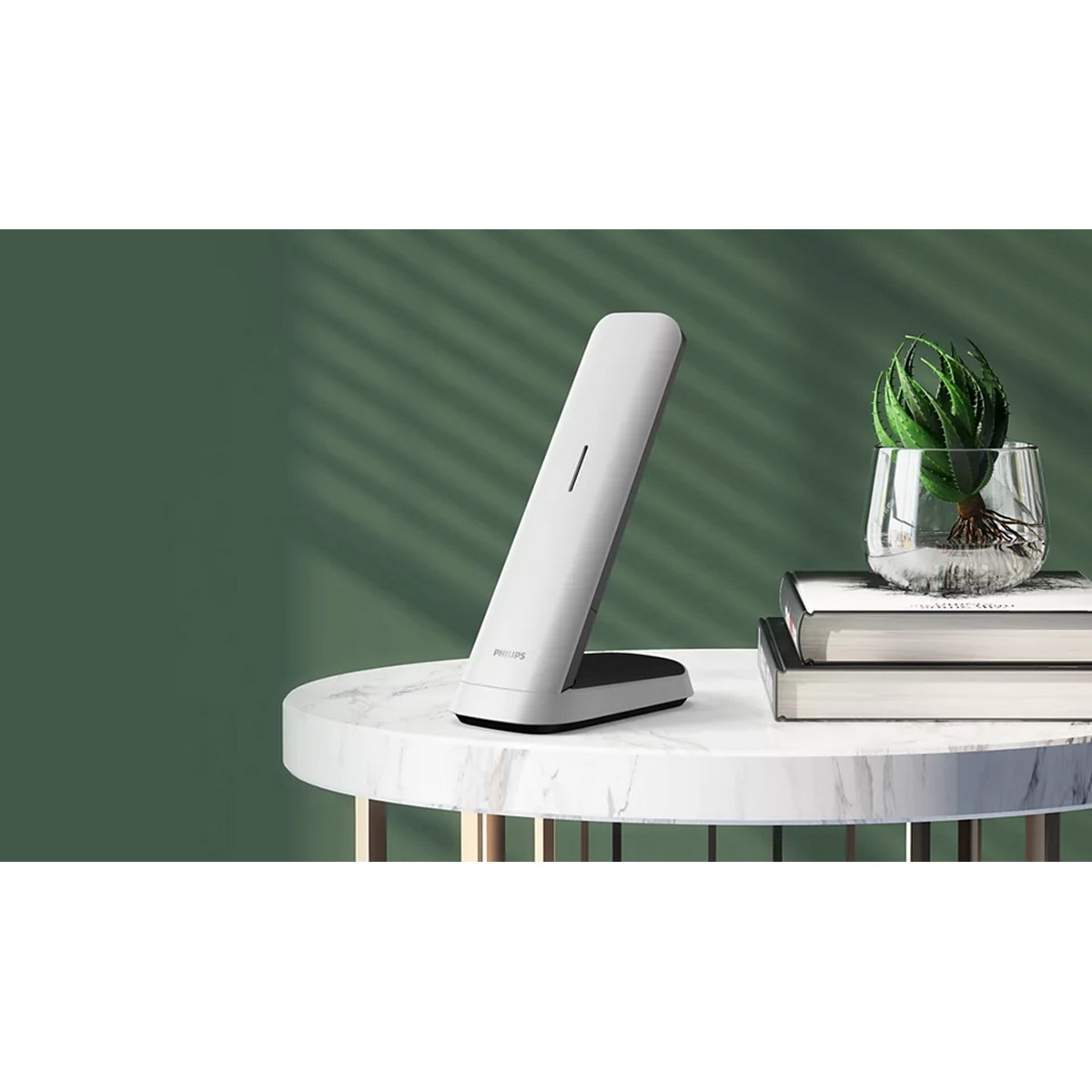 Un cargador inalámbrico Philips blanco con un teléfono en una mesa. Fondo verde.