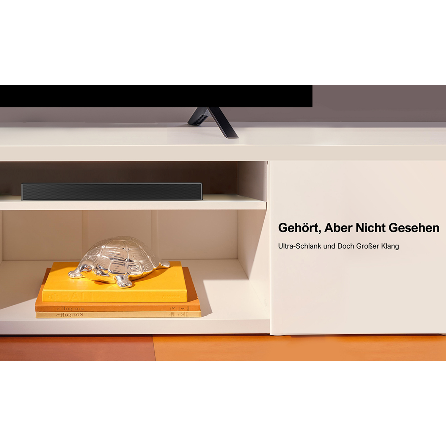 Eine schwarze Soundbar liegt auf einem Regal mit einer Schildkrötenfigur und Büchern. Ein Fernseher ist oben.