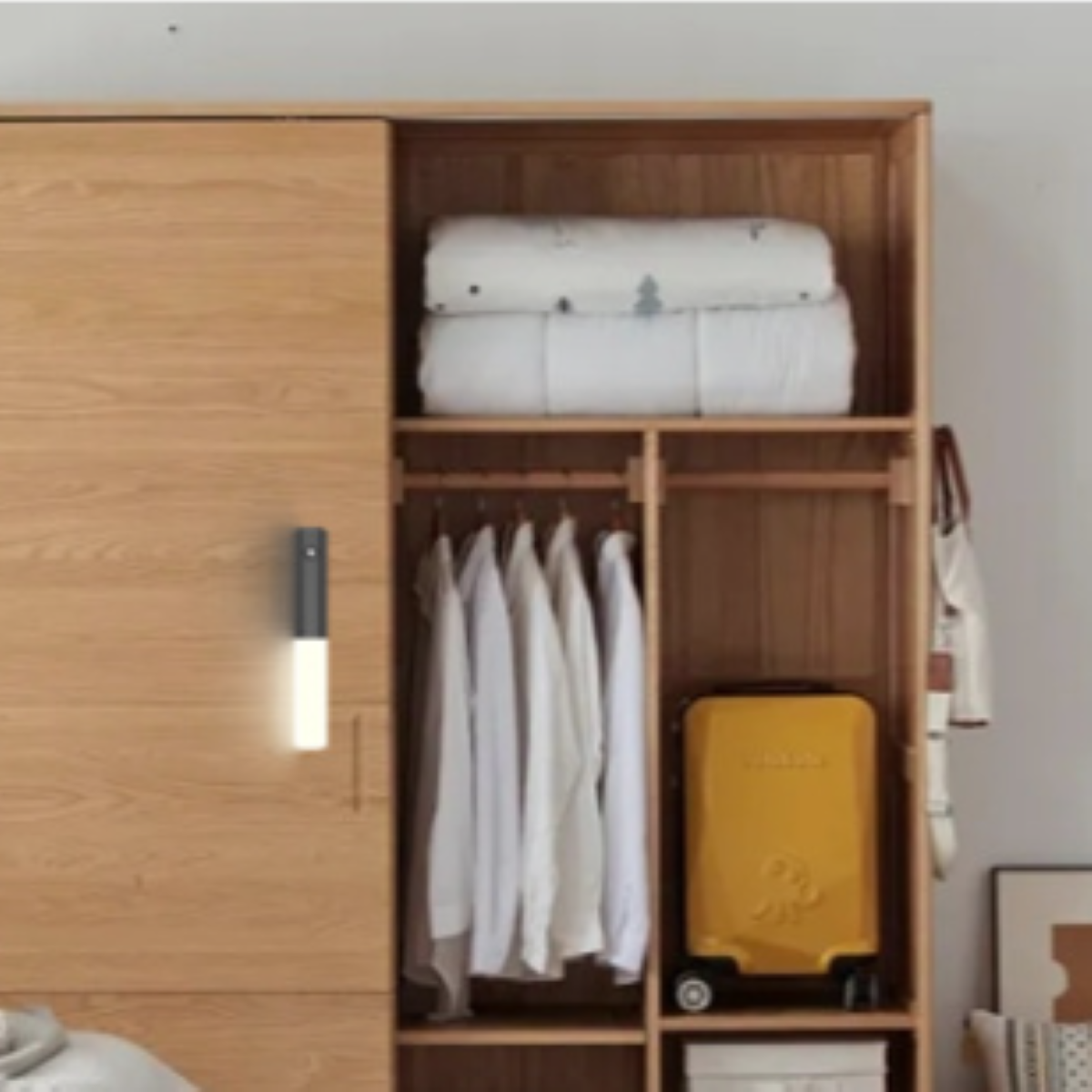 Holzschrank mit gestapelten Decken, hängenden Hemden und einem gelben Koffer.