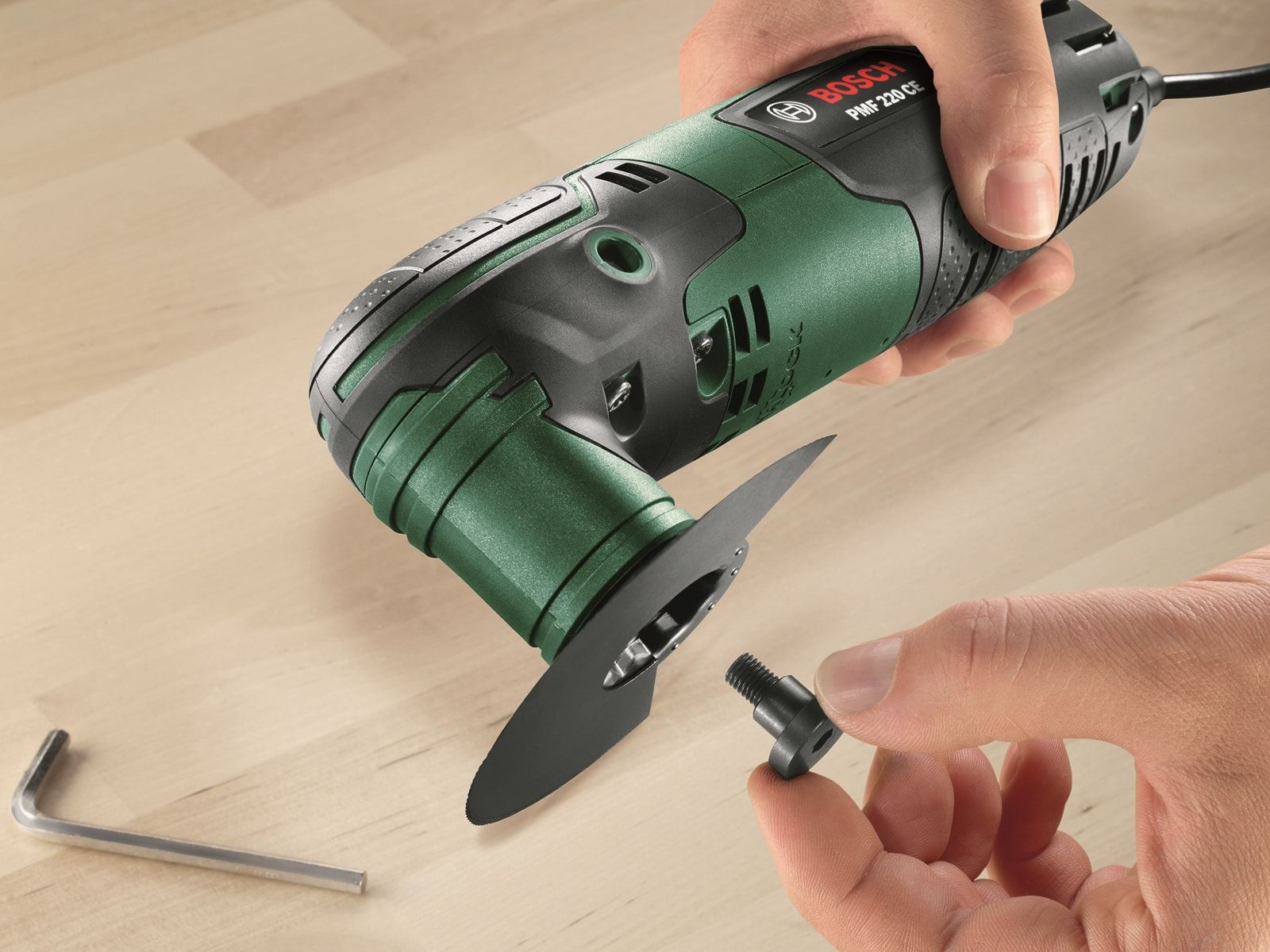 Zielone i czarne elektronarzędzie z ostrzem. Dłoń trzyma śrubę w pobliżu ostrza, a klucz leży na drewnie.