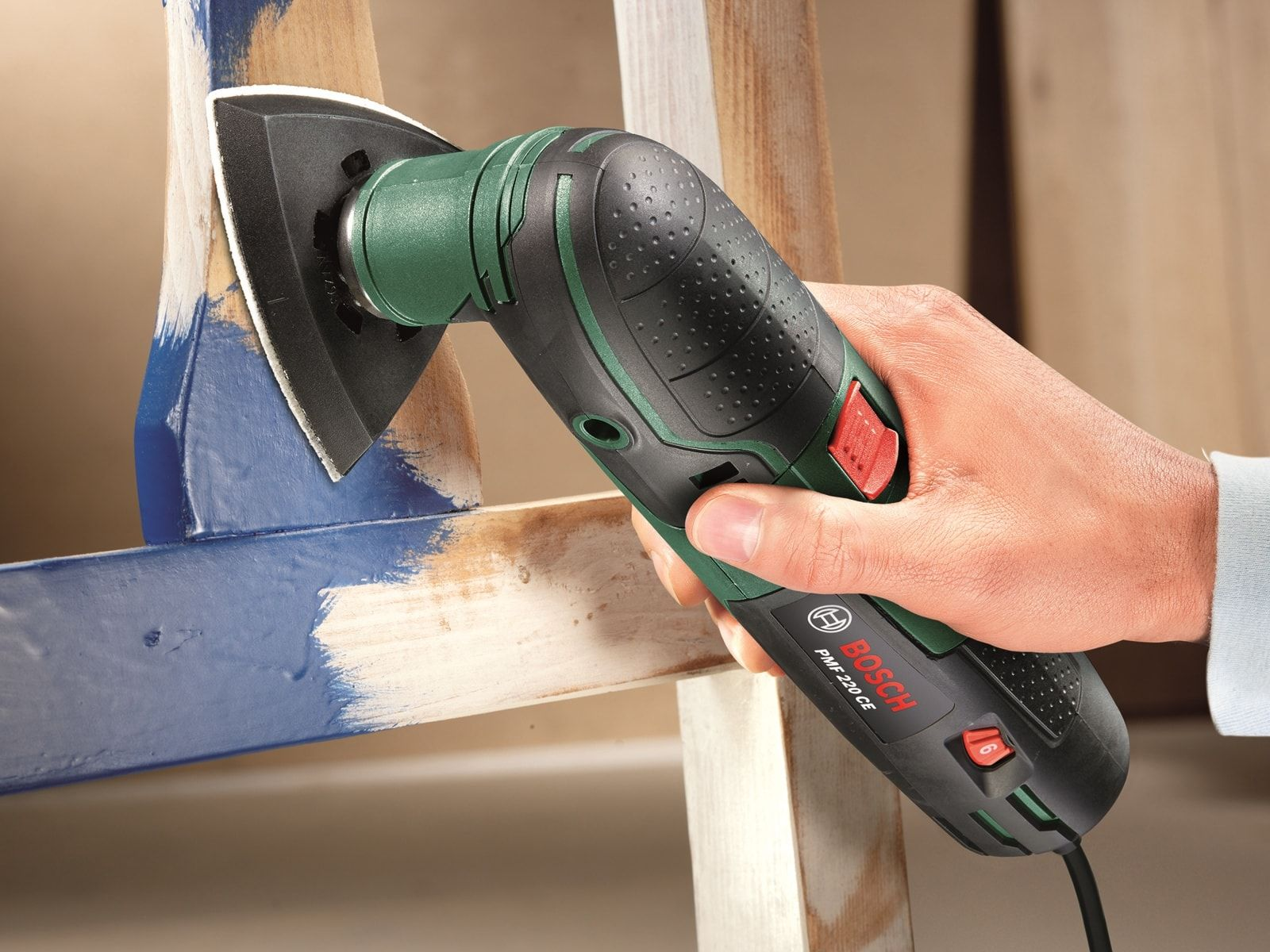 Dłoń używa narzędzia wielofunkcyjnego do szlifowania nogi drewnianego krzesła.