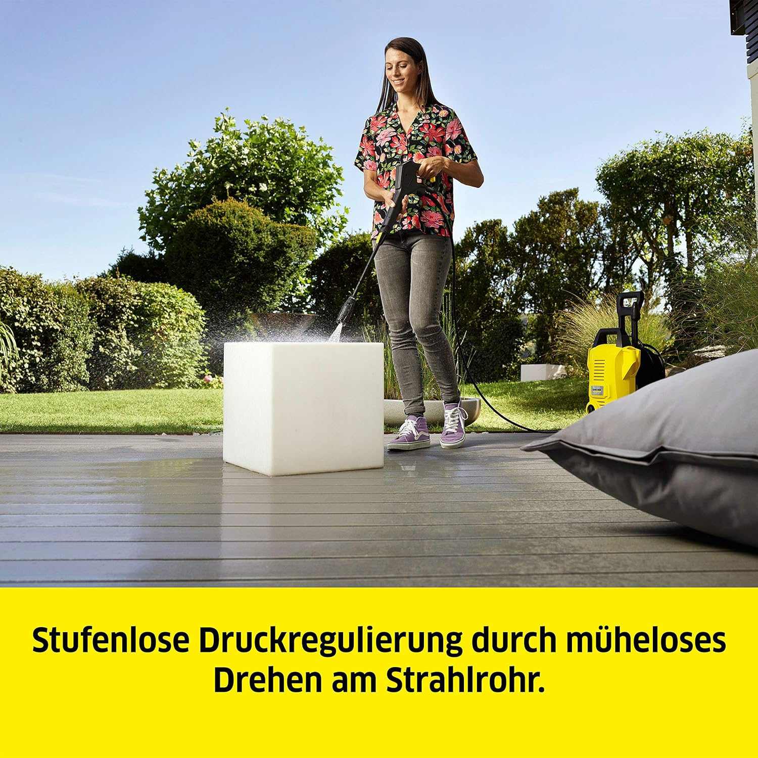 Kobieta używa myjki ciśnieniowej do czyszczenia białego bloku. Tekst: Regulacja ciśnienia przez obracanie lancy.