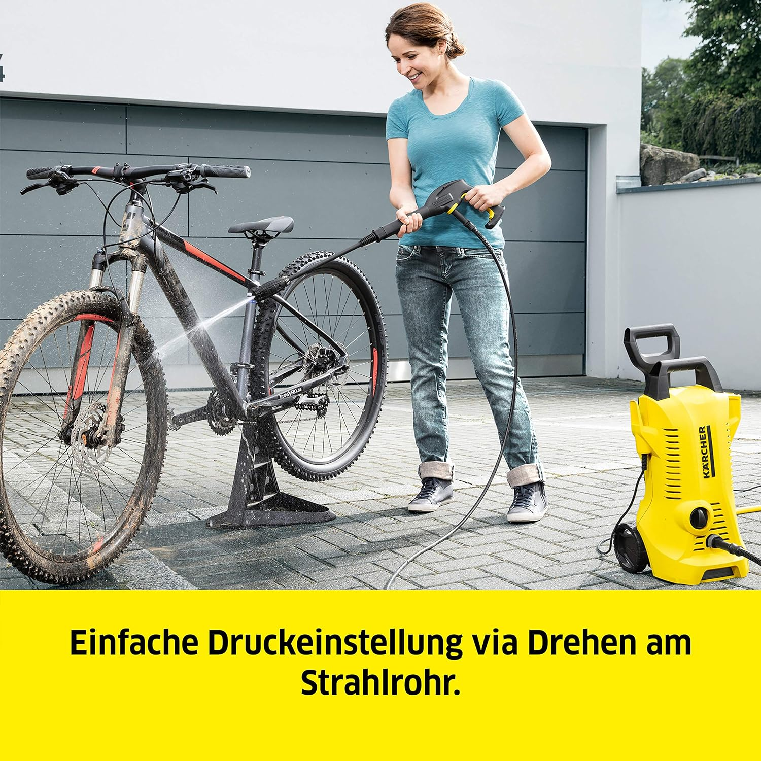 Eine Frau wäscht ein Mountainbike mit einem gelben Hochdruckreiniger.